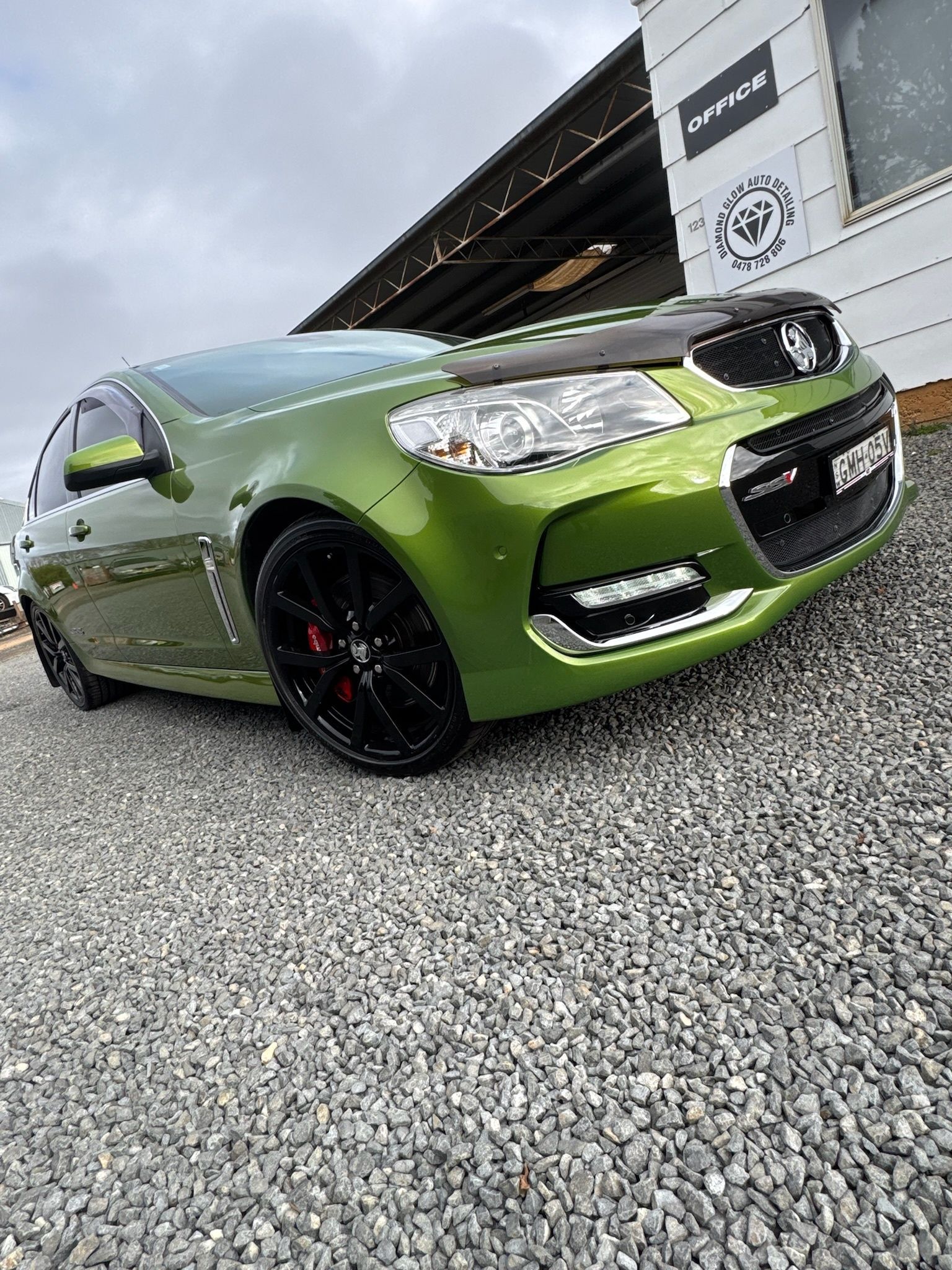 Green sedan parked on gravel outside a building, angled front view with black rims.