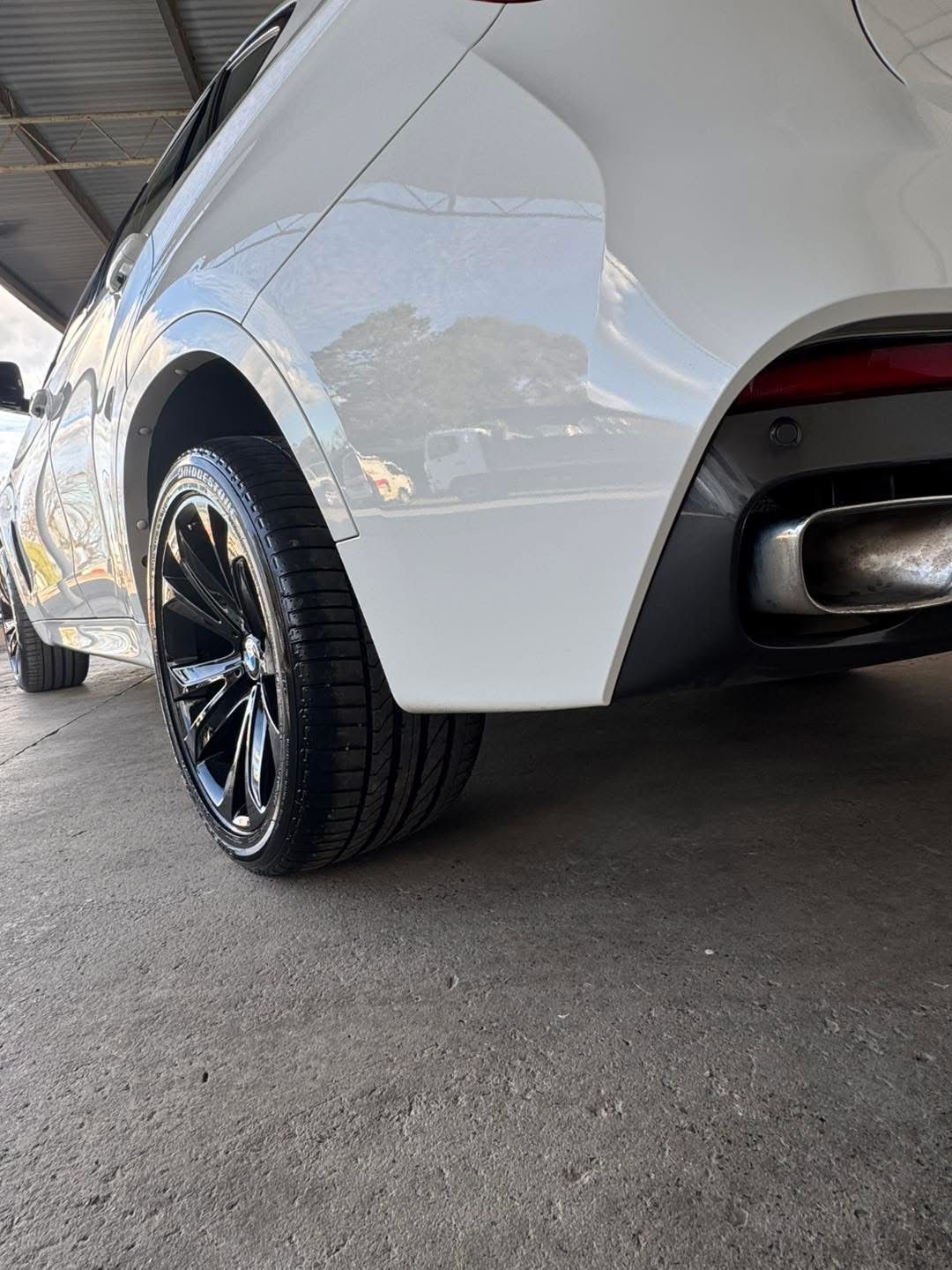 Close-up of a white car’s rear wheel and bumper parked on pavement under cover - — Diamond Glow Auto Detailing in Armidale, NSW