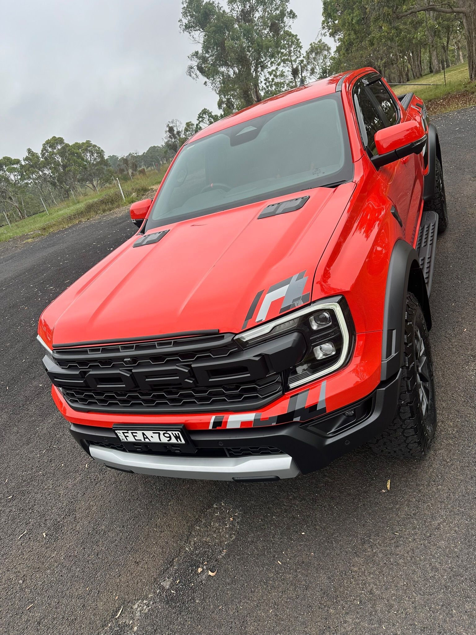 Red pickup truck driving on a wet road in the rain, viewed from the front-left side.