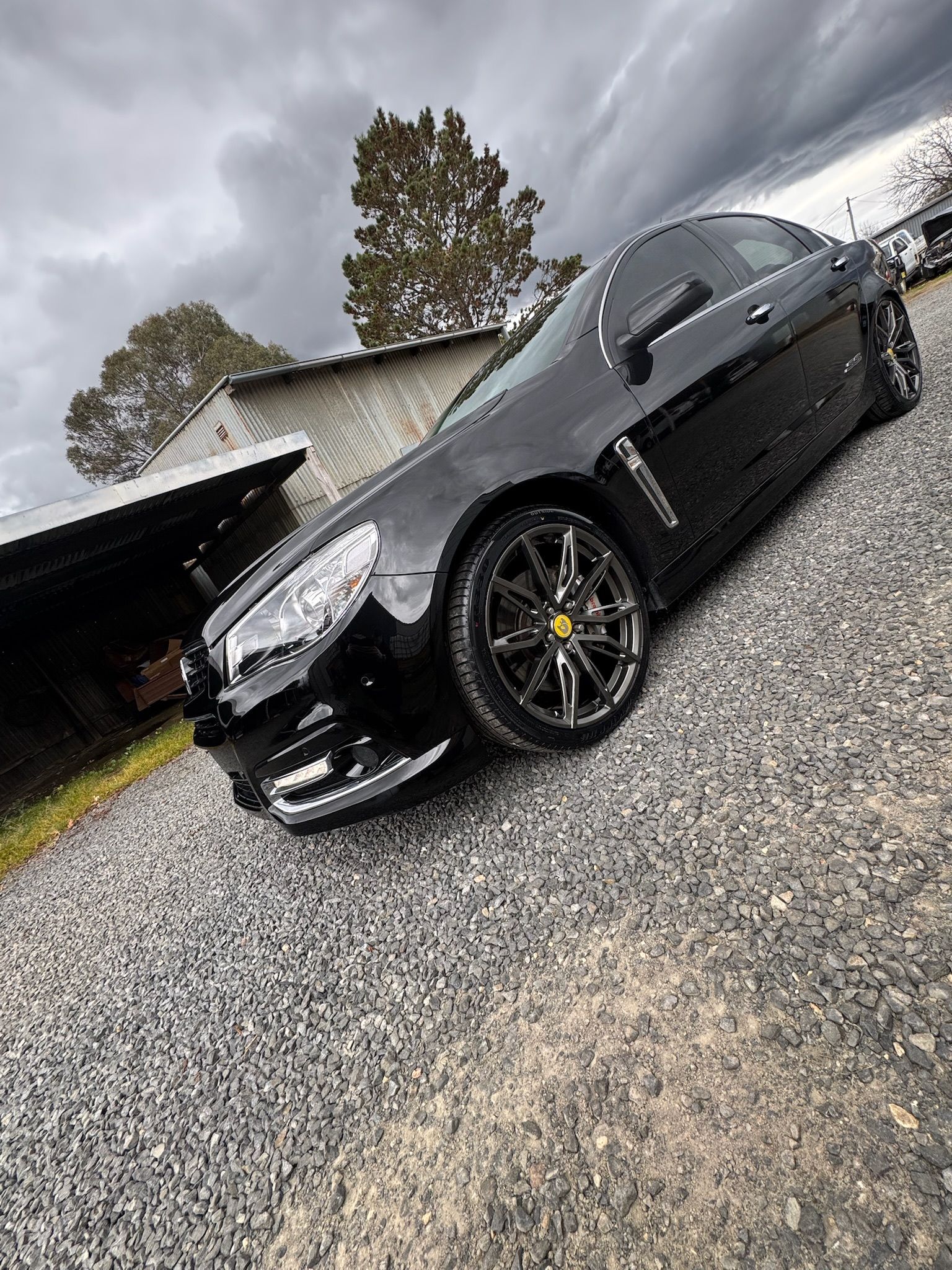 Black sedan parked on gravel beside a house on a cloudy day