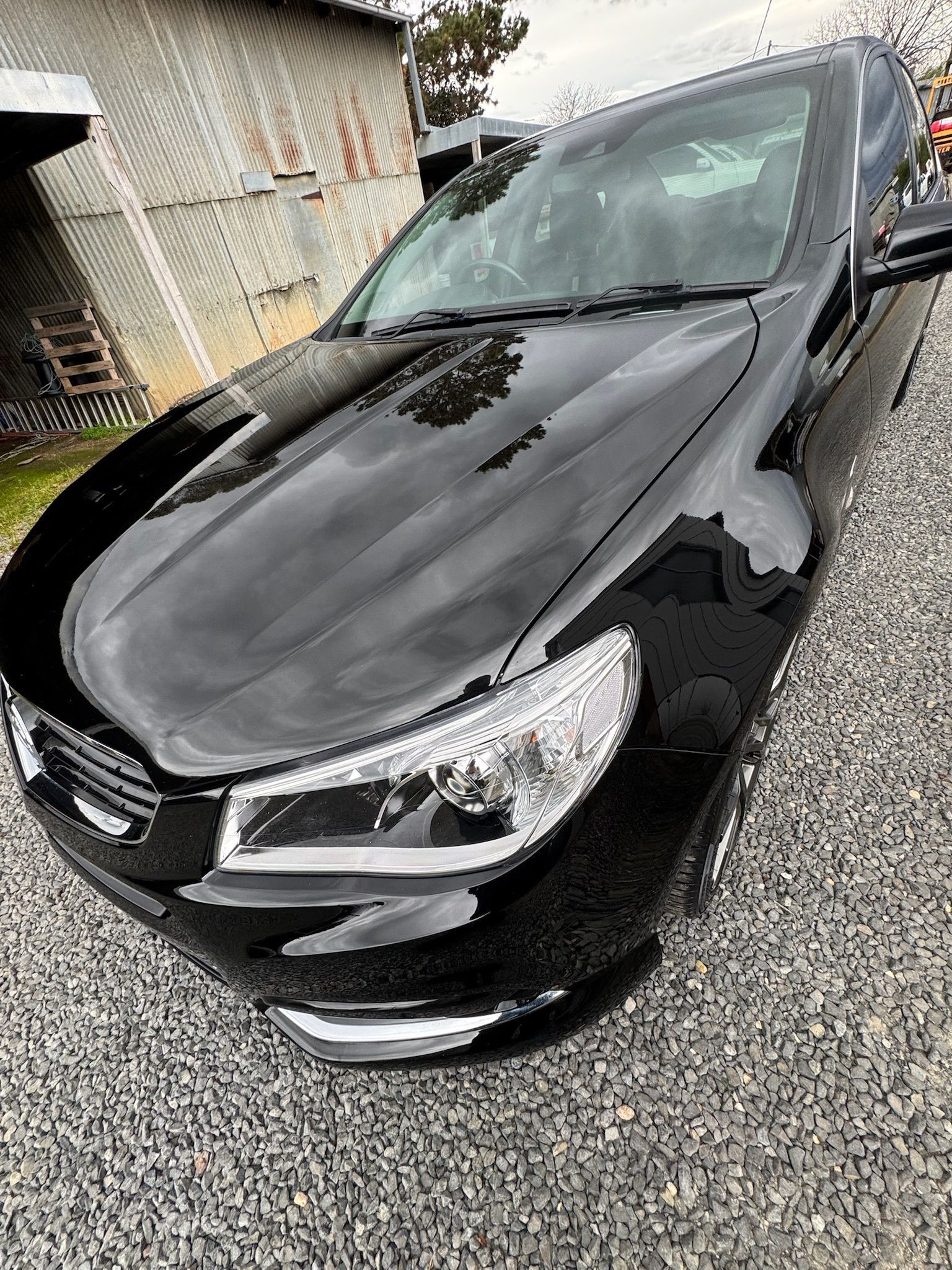 Black sedan parked on gravel beside a house, front-left view with visible windshield damage