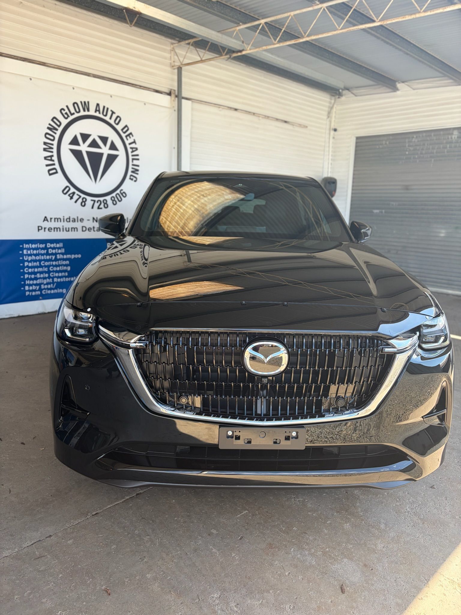 Black Mazda SUV parked indoors in front of a wall logo.