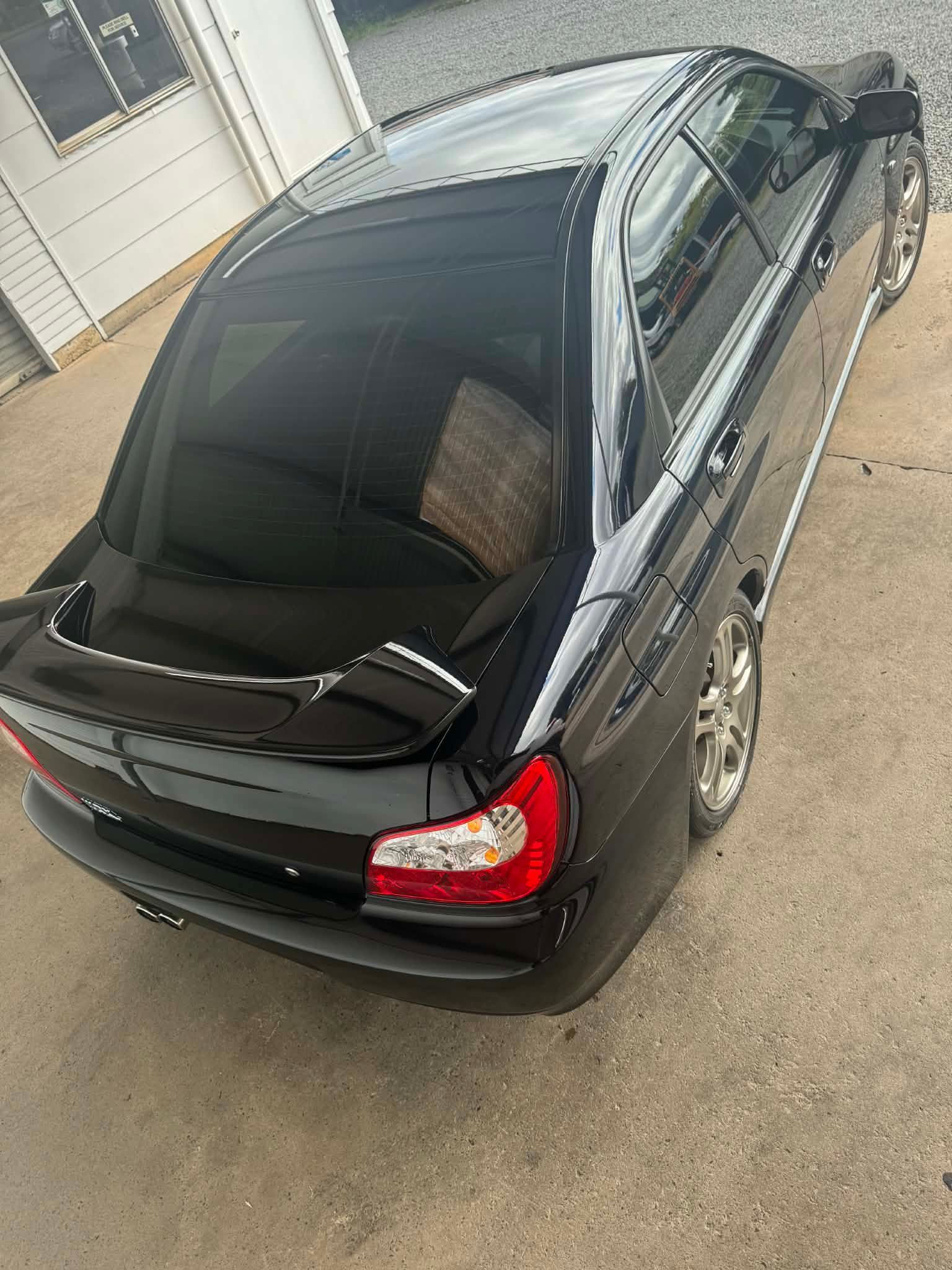 Black sedan parked in a driveway, viewed from above, with tinted windows and chrome trim.