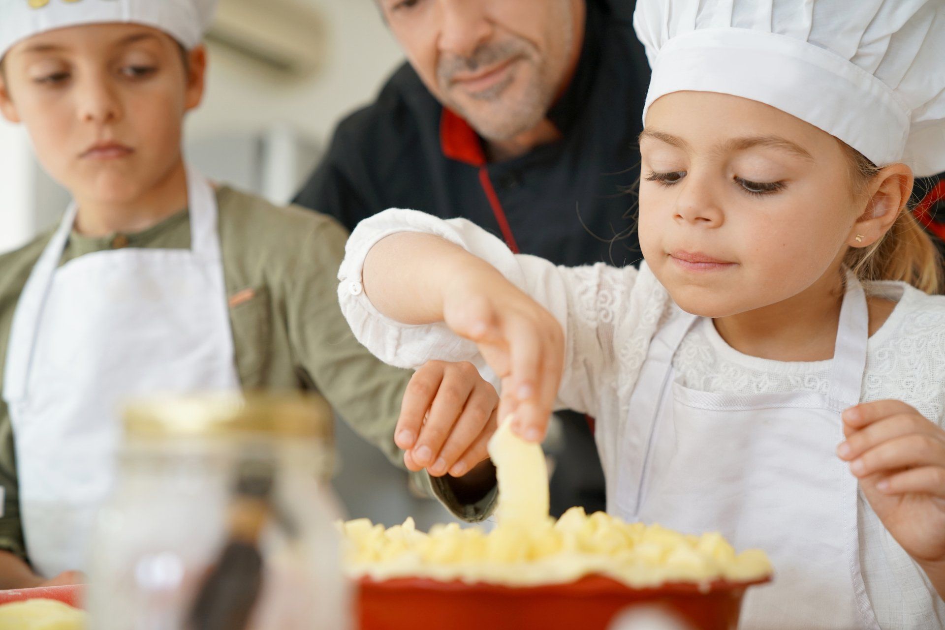 Children and an adult baking together, frosting a dessert in a kitchen