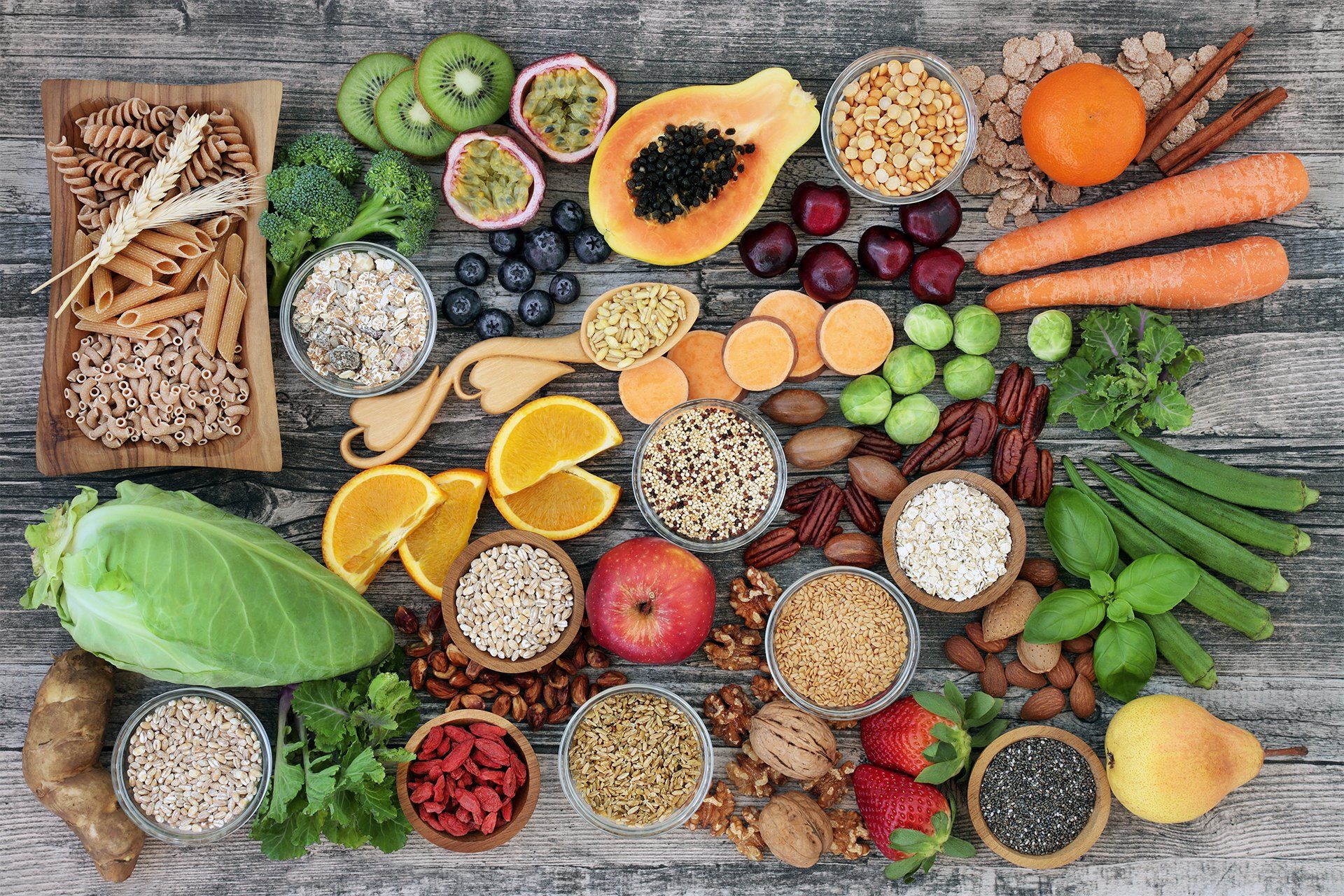 Assorted fresh fruits, vegetables, grains, and nuts arranged on a rustic wooden table.