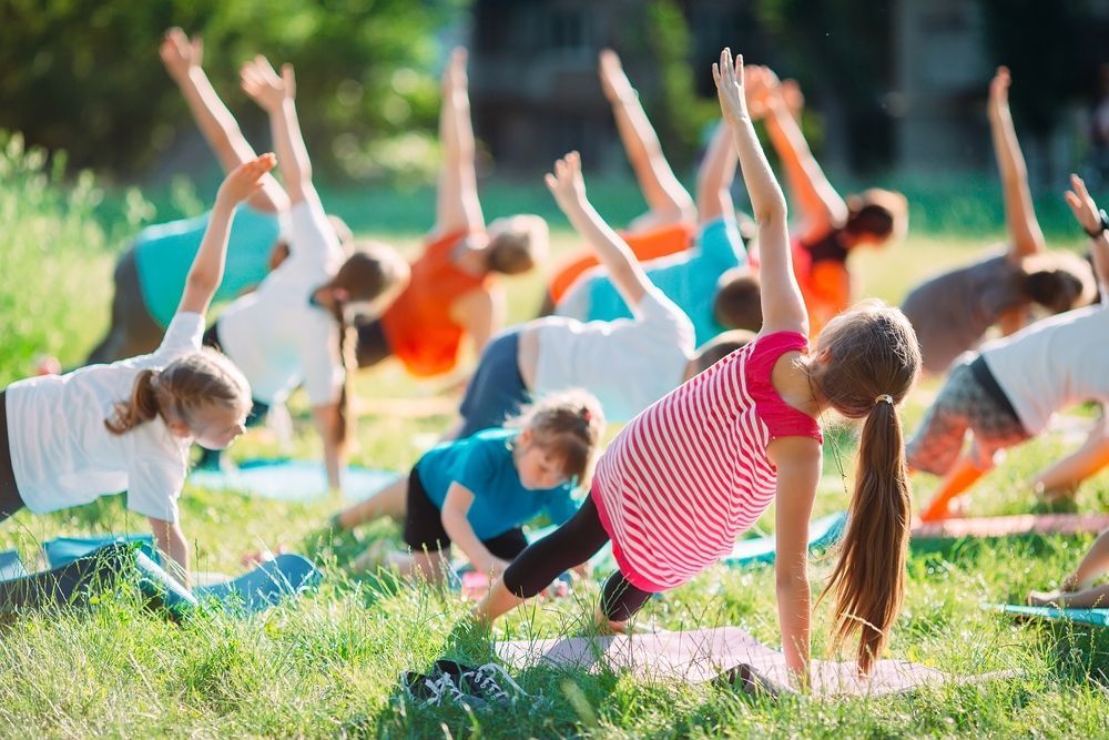 People stretching on mats in a grassy park during outdoor exercise class
