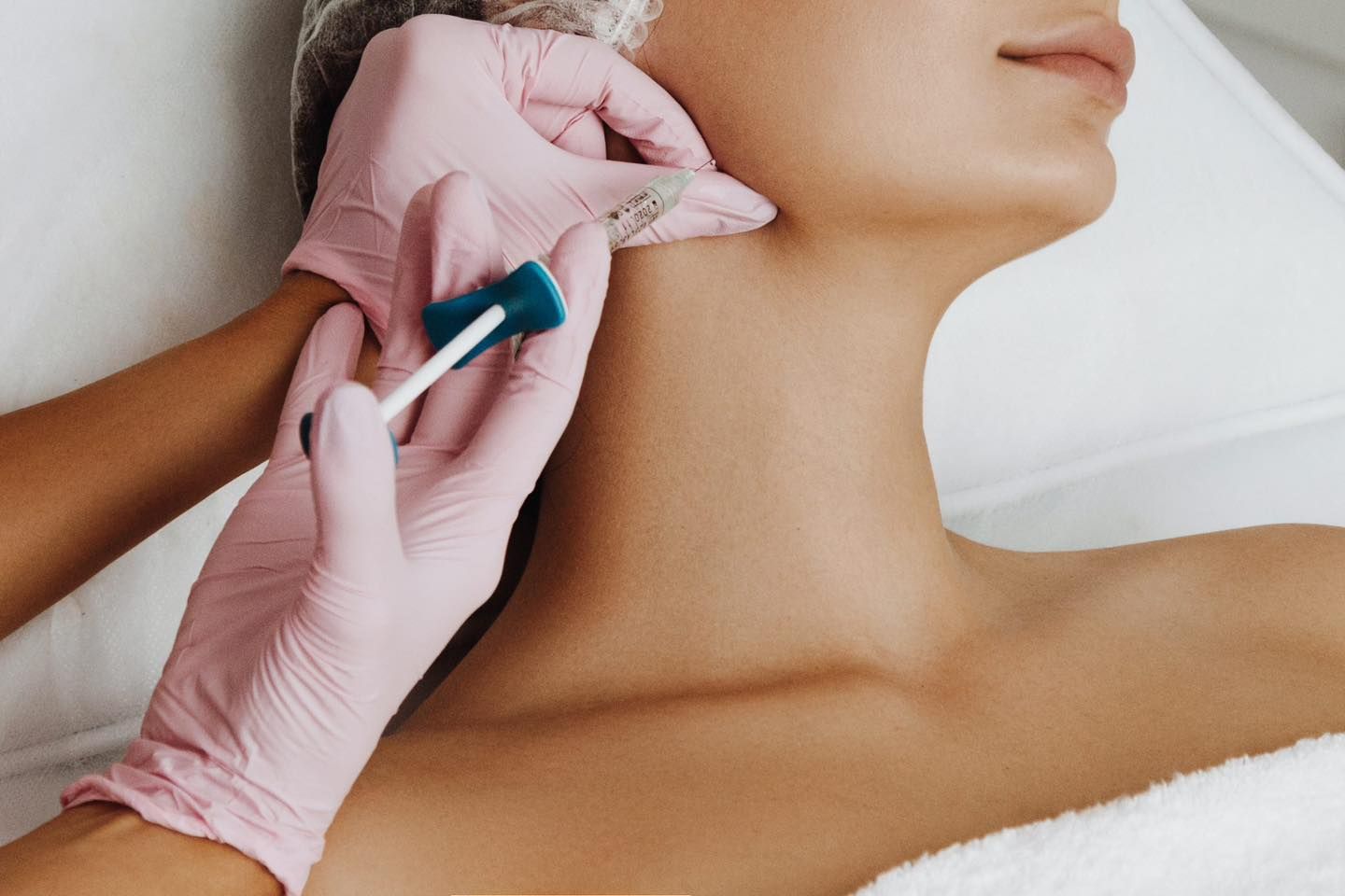 Una persona con i guanti rosa somministra un'iniezione cosmetica nella mandibola di un paziente sdraiato su un lettino medico.