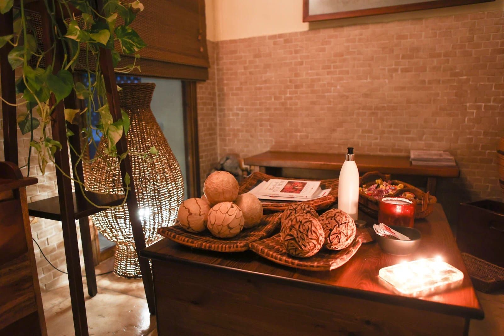 Un'area relax spa dai toni caldi con decorazioni intrecciate, un tavolino in legno su cui sono appoggiate sfere decorative, una candela e una pianta.