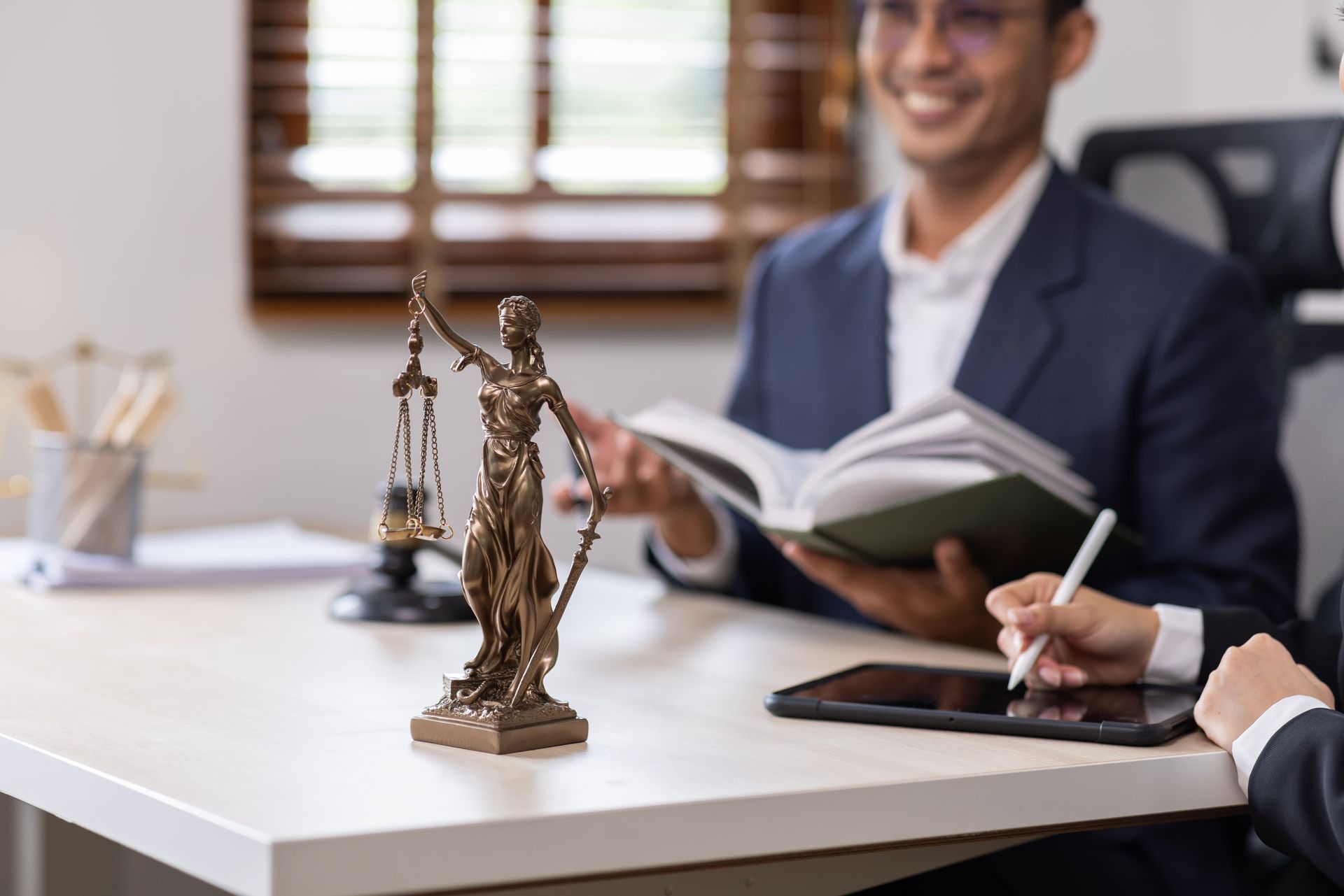 Lawyers reviewing documents at a desk, Lady Justice statue in foreground.