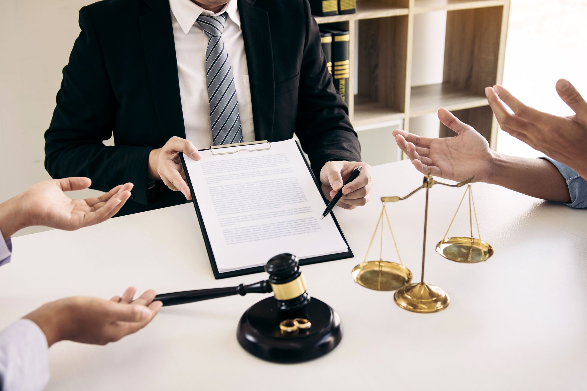 Lawyer presenting document to two people, gavel and scales on desk, office setting.