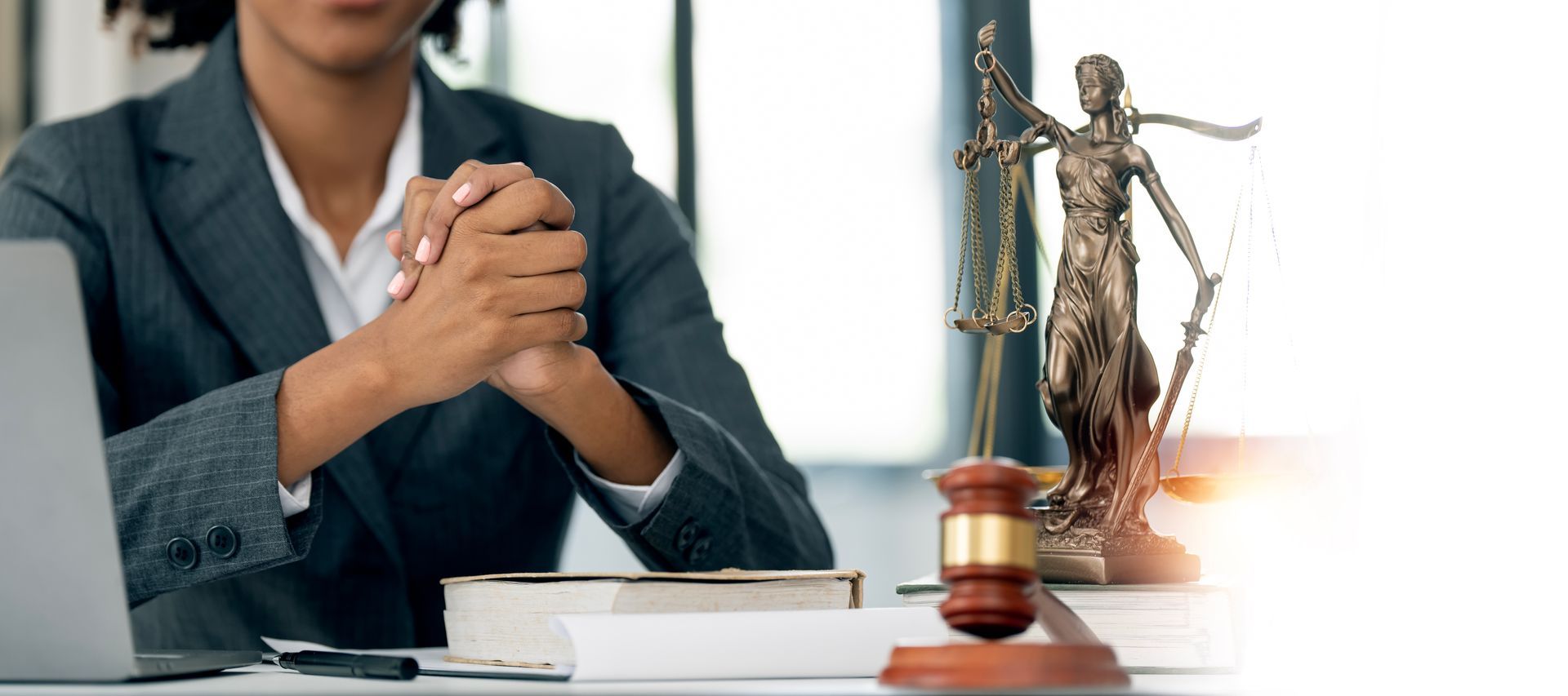 Person in a suit with hands clasped, next to a gavel and Lady Justice statue.