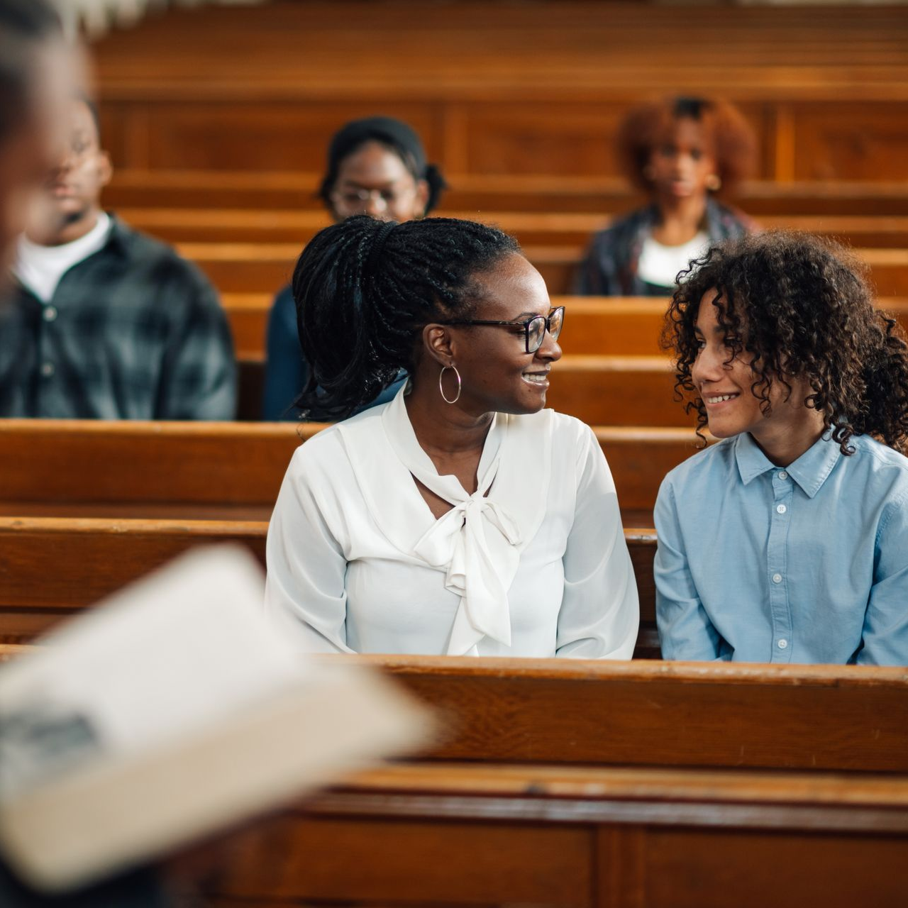 Woman and child smiling at each other in a church pew; other people seated behind them.