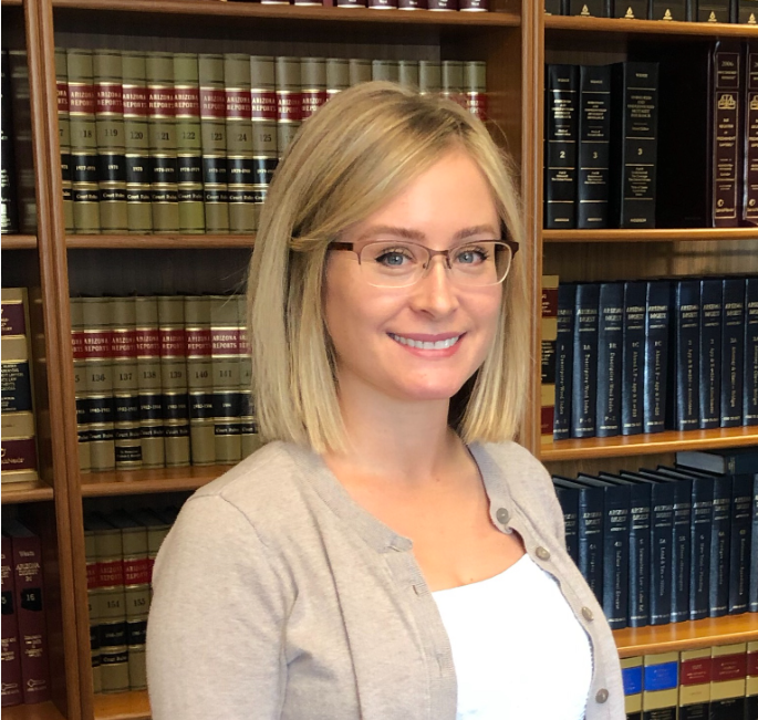 Woman with blonde hair and glasses smiles in front of bookshelves filled with law books.