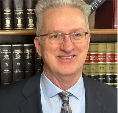 Man in suit and glasses smiling in front of a bookshelf filled with legal books.