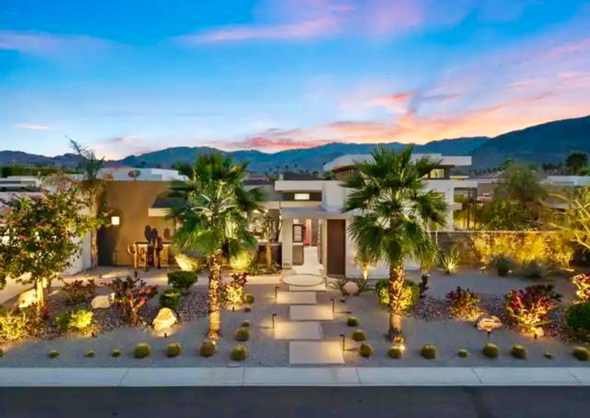 Modern house at dusk with lit palm trees, desert landscaping, and mountains in the background