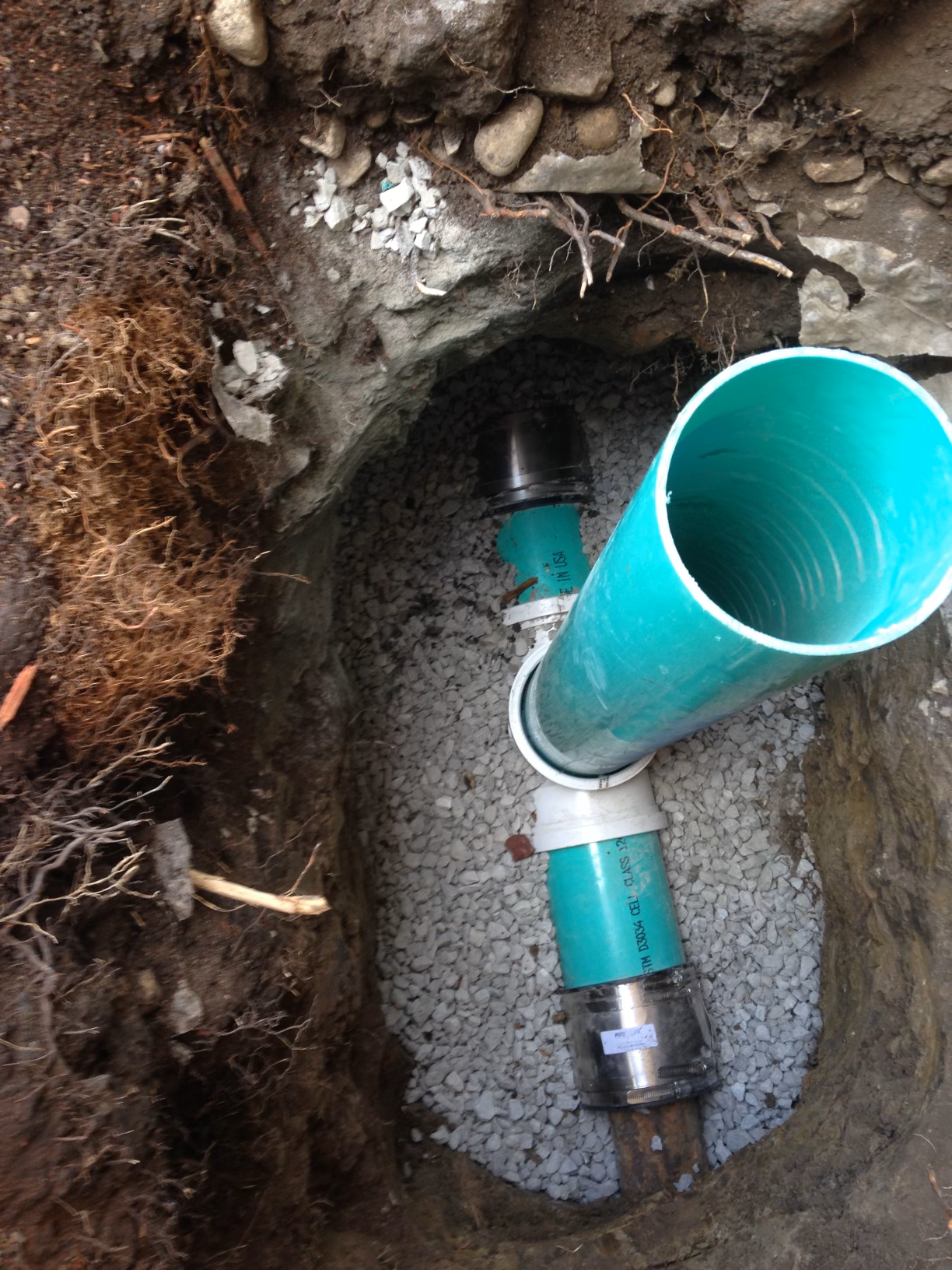 Open utility pit with blue PVC pipes and gravel inside the ground