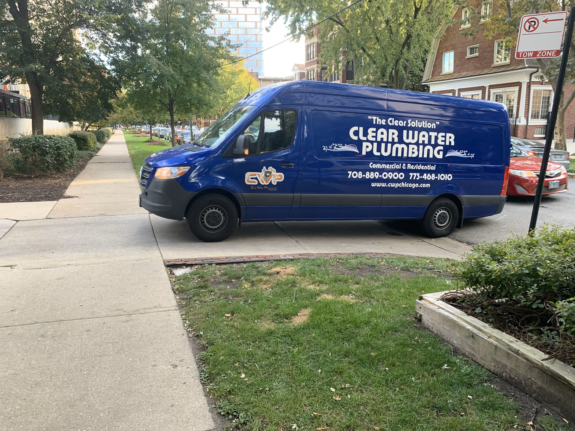 Blue Clear Water Plumbing van parked by a sidewalk in a leafy residential area