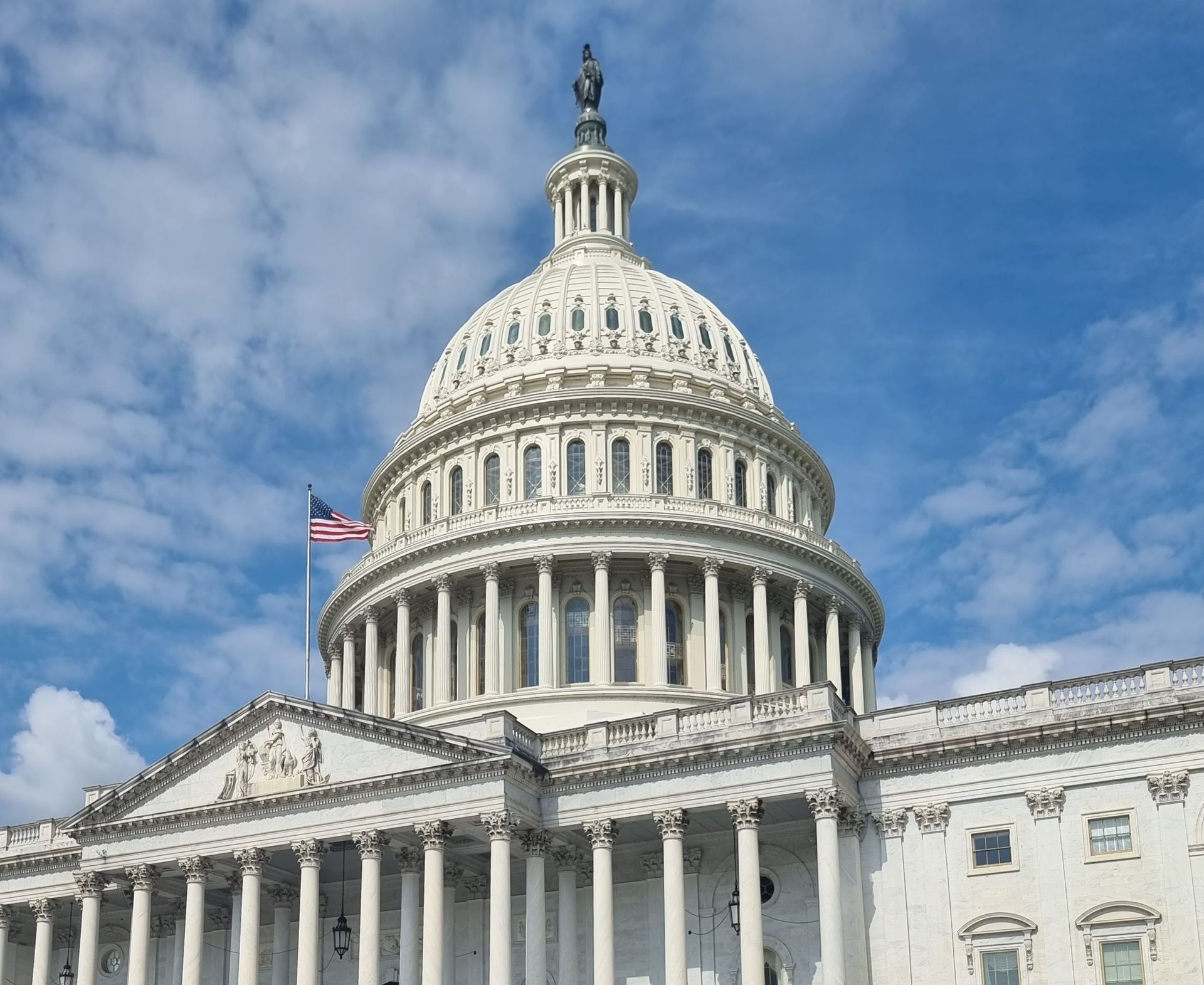 U.S. Capitol dome and columns against a blue sky, with an American flag visible