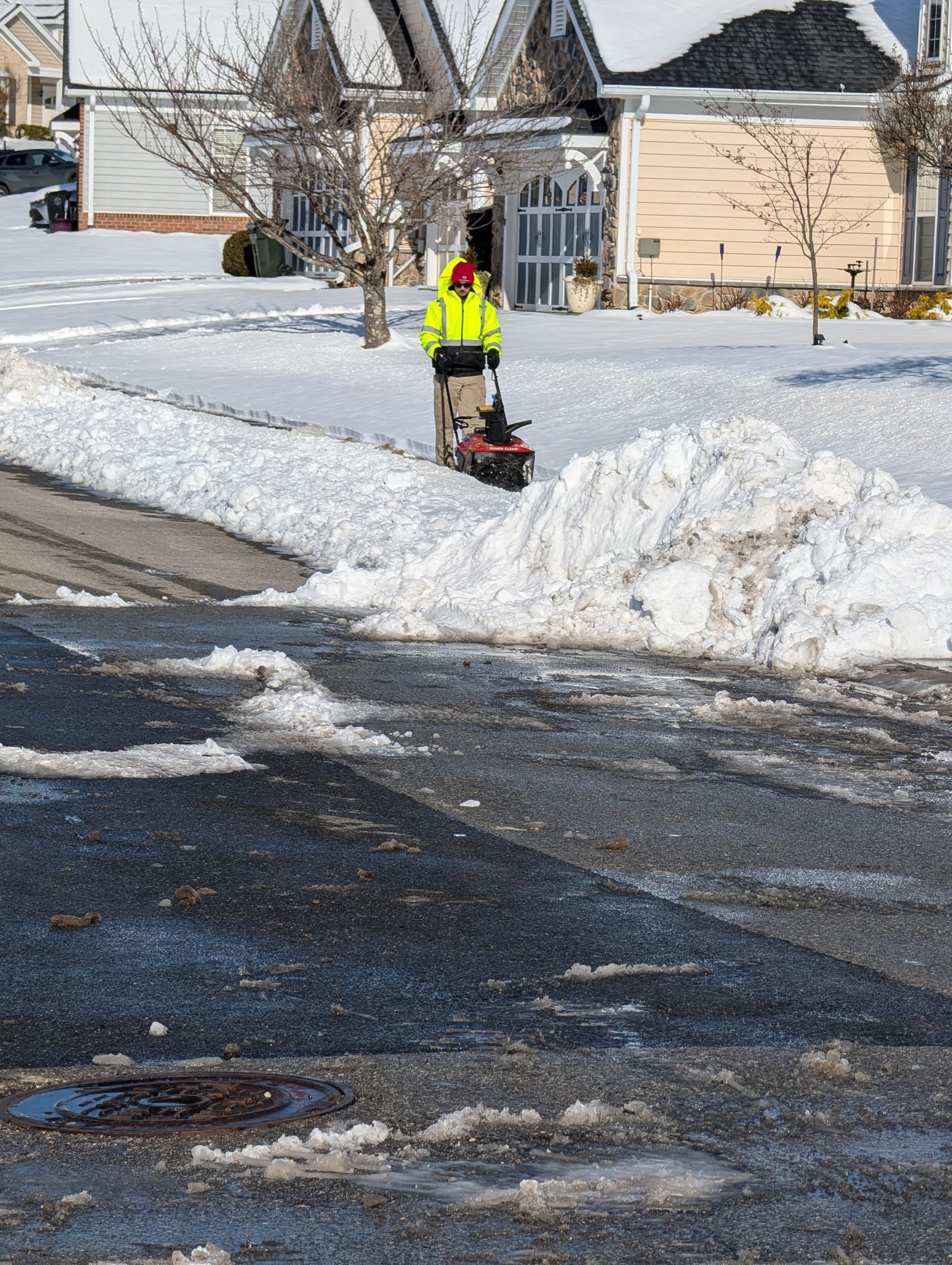 A man is using a snow blower to clear snow from the sidewalk.