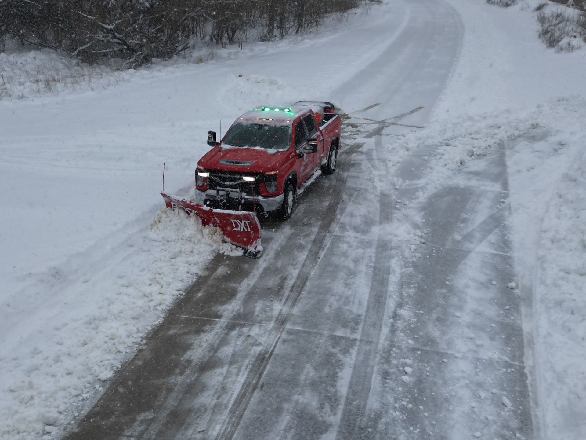 A red truck is plowing snow on a snowy road.