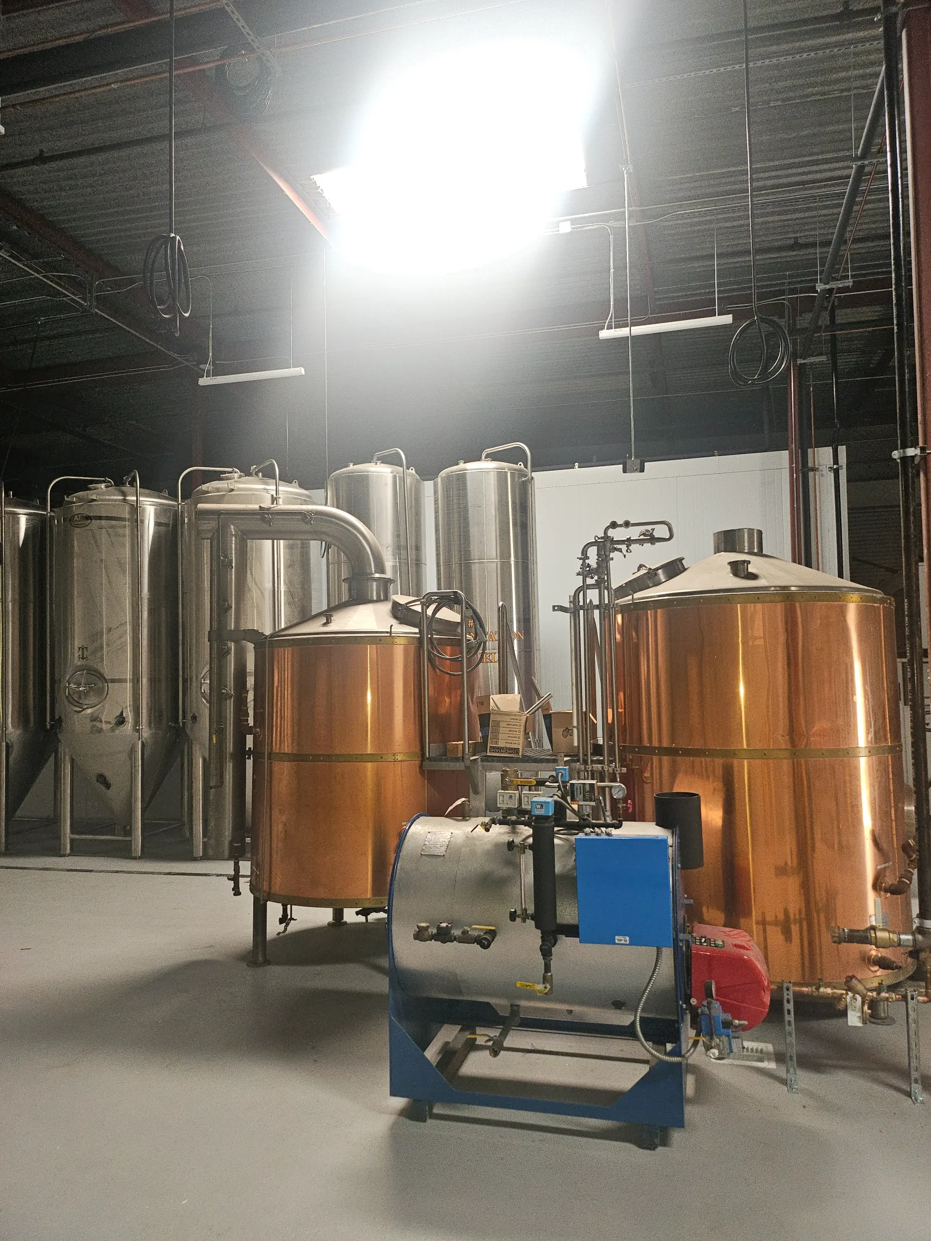 A industrial brewery interior featuring copper brew kettles and stainless steel fermentation tanks.