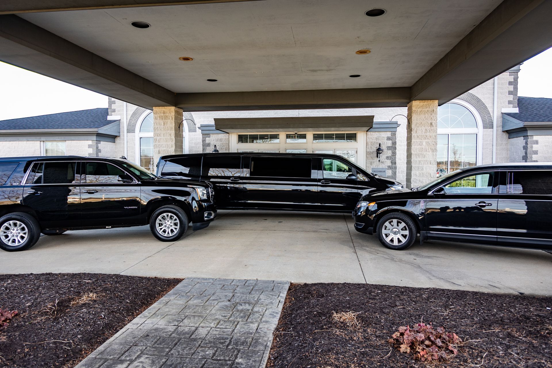 Three black cars are parked under a covered walkway in front of a building.