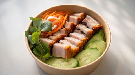 A Vietnamese banh mi sandwich with meat, fresh cilantro, and chili slices on parchment paper, with a bowl in the background.