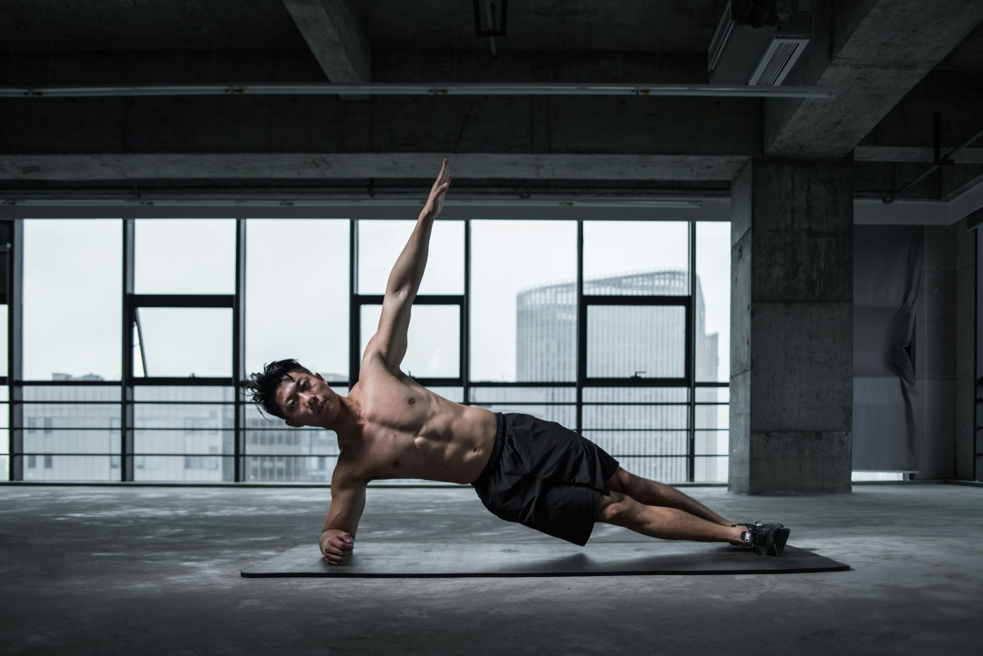 Man doing side plank with arm raised in urban setting.