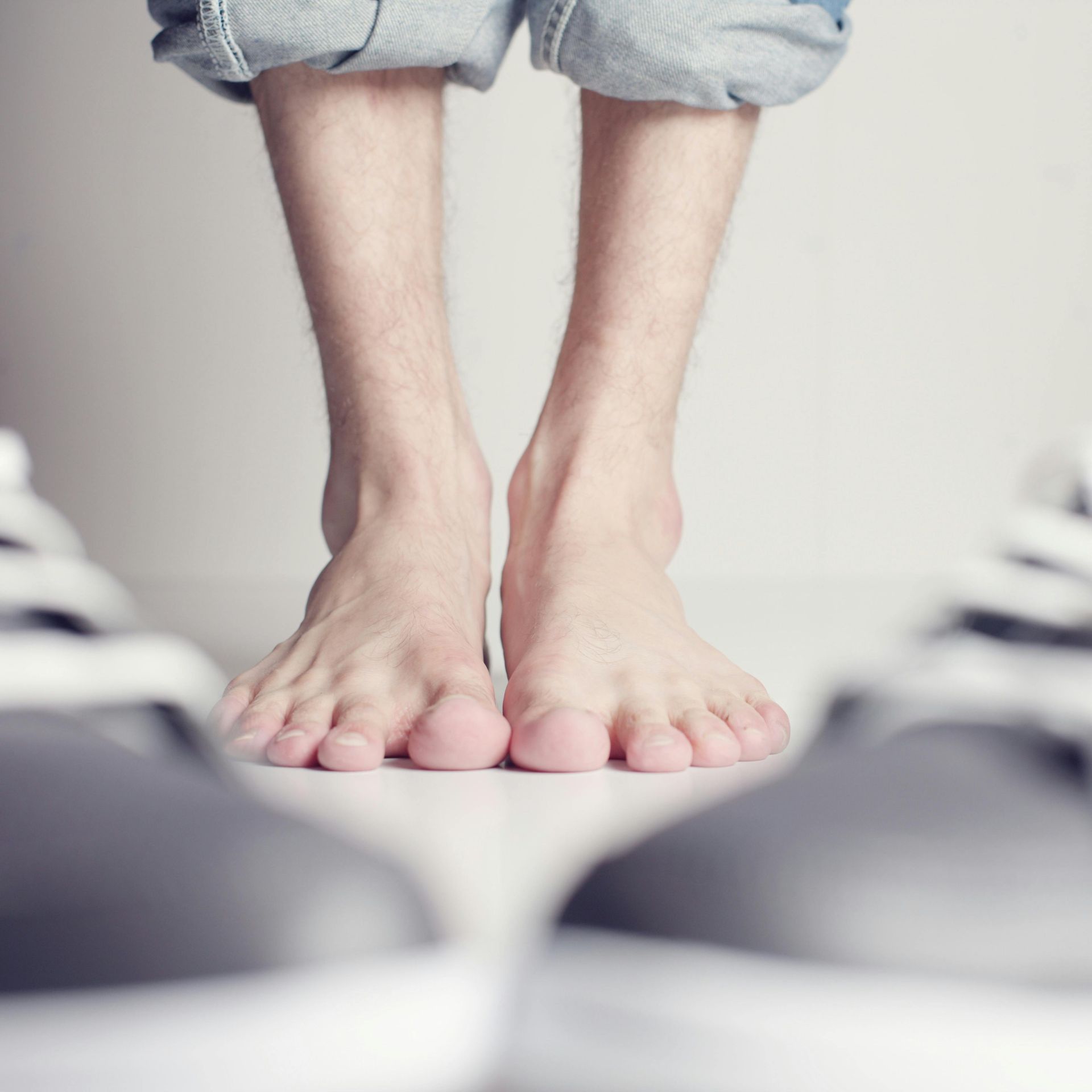 Bare feet stand between two gray sneakers on a white floor.