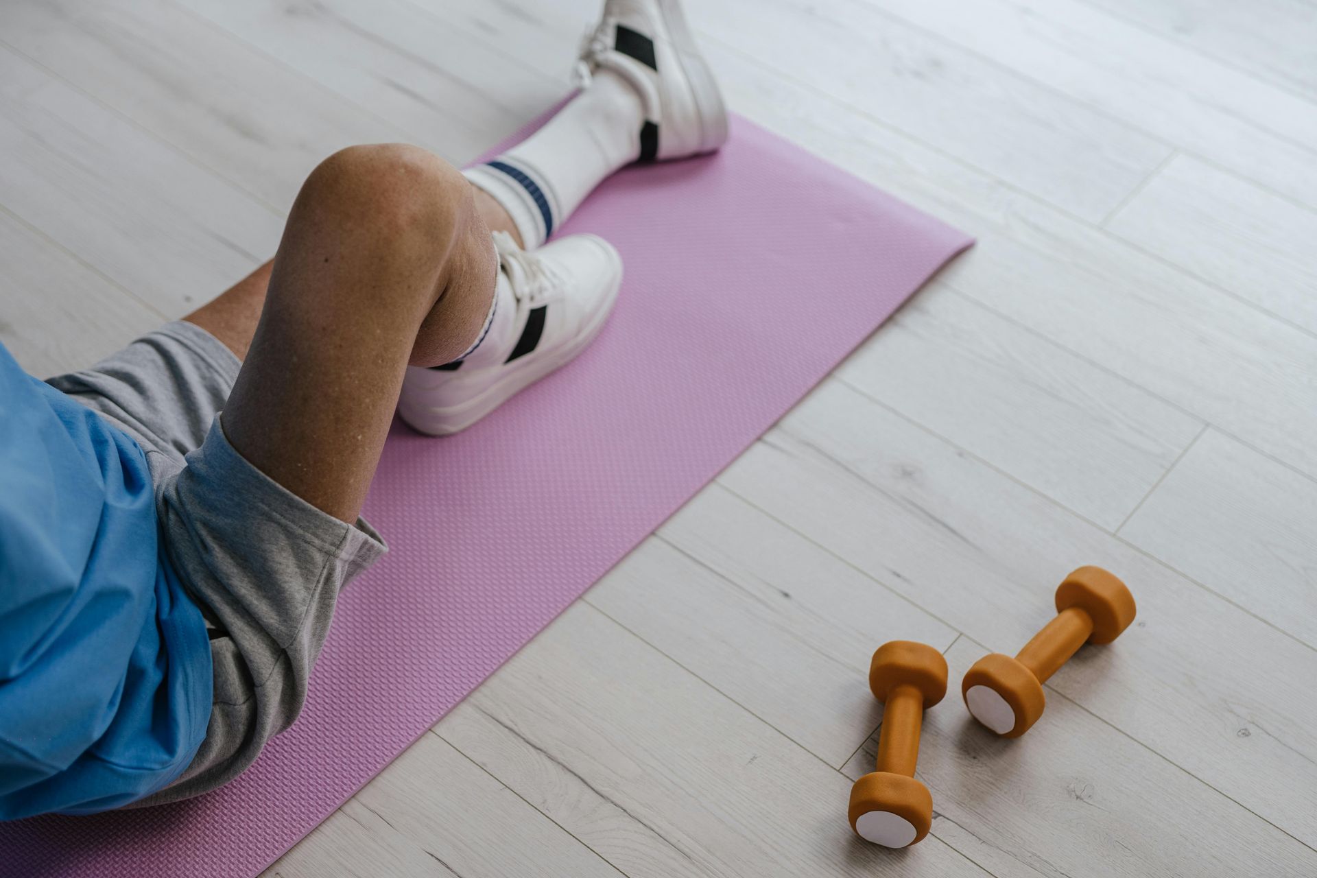 Person on a pink exercise mat with dumbbells on a light wood floor.