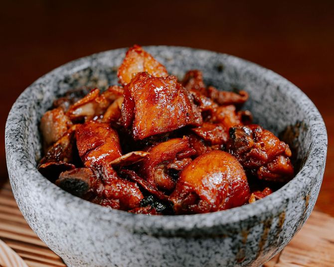 Dark glazed stir-fried meat in a gray stone bowl on a wooden table