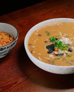 Two bowls on a wooden table, one with orange soup garnished with herbs and seaweed, one with rice.