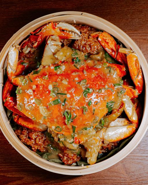 Bowl of crab covered in spicy red sauce with green herbs on a wooden table