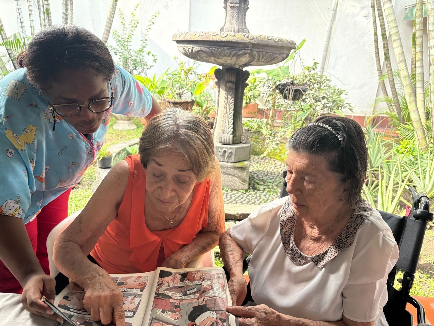 Tres mujeres se inclinan sobre un álbum de fotos en una mesa al aire libre y miran fotos antiguas.