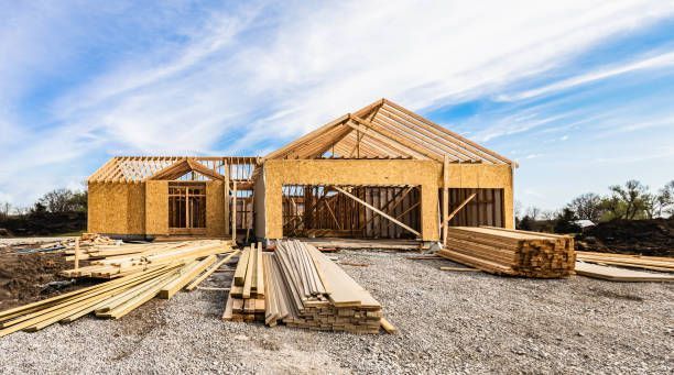 House under construction, wood framing visible, outdoors, bright sky.