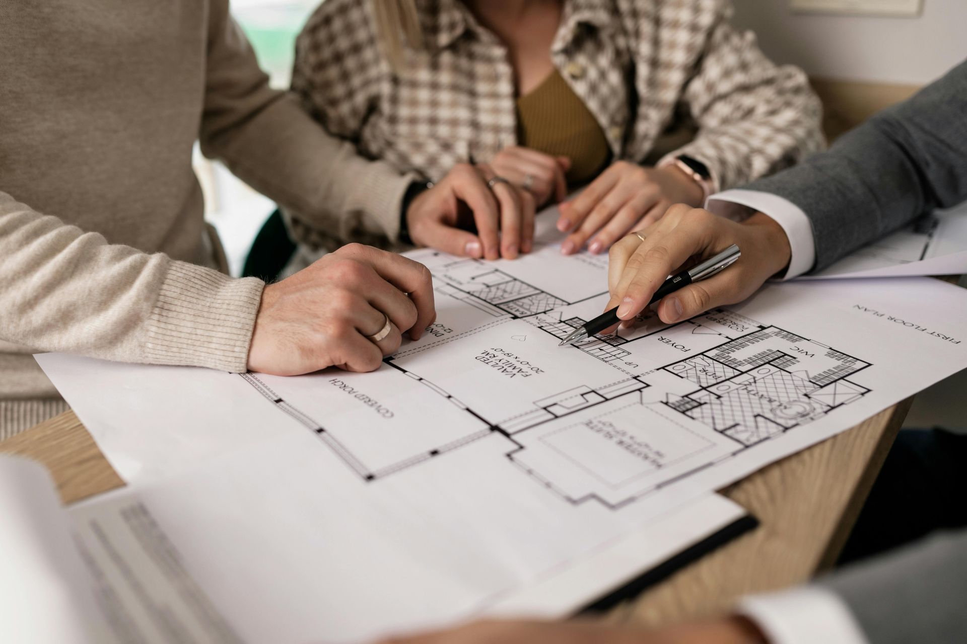 A person points at architectural plans while two others look on; seated around a table.