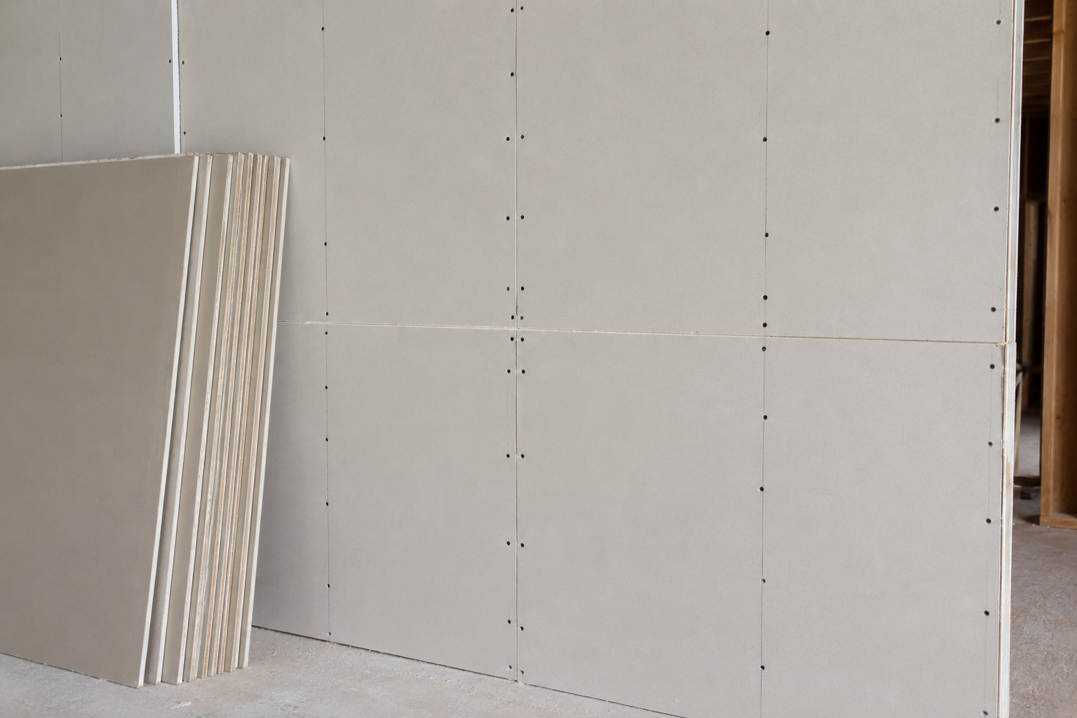 Drywall sheets stacked against a partially finished interior wall with visible screw marks.