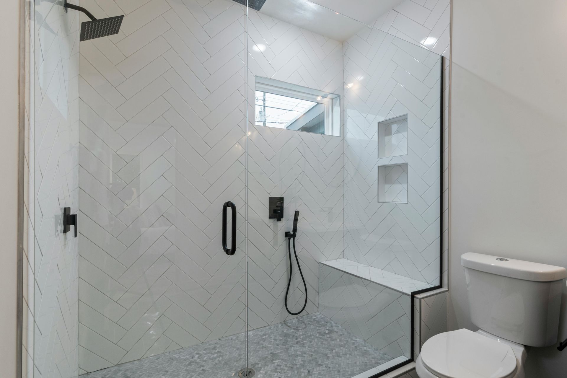 Bright white tiled bathroom with a glass shower door and a toilet in the foreground