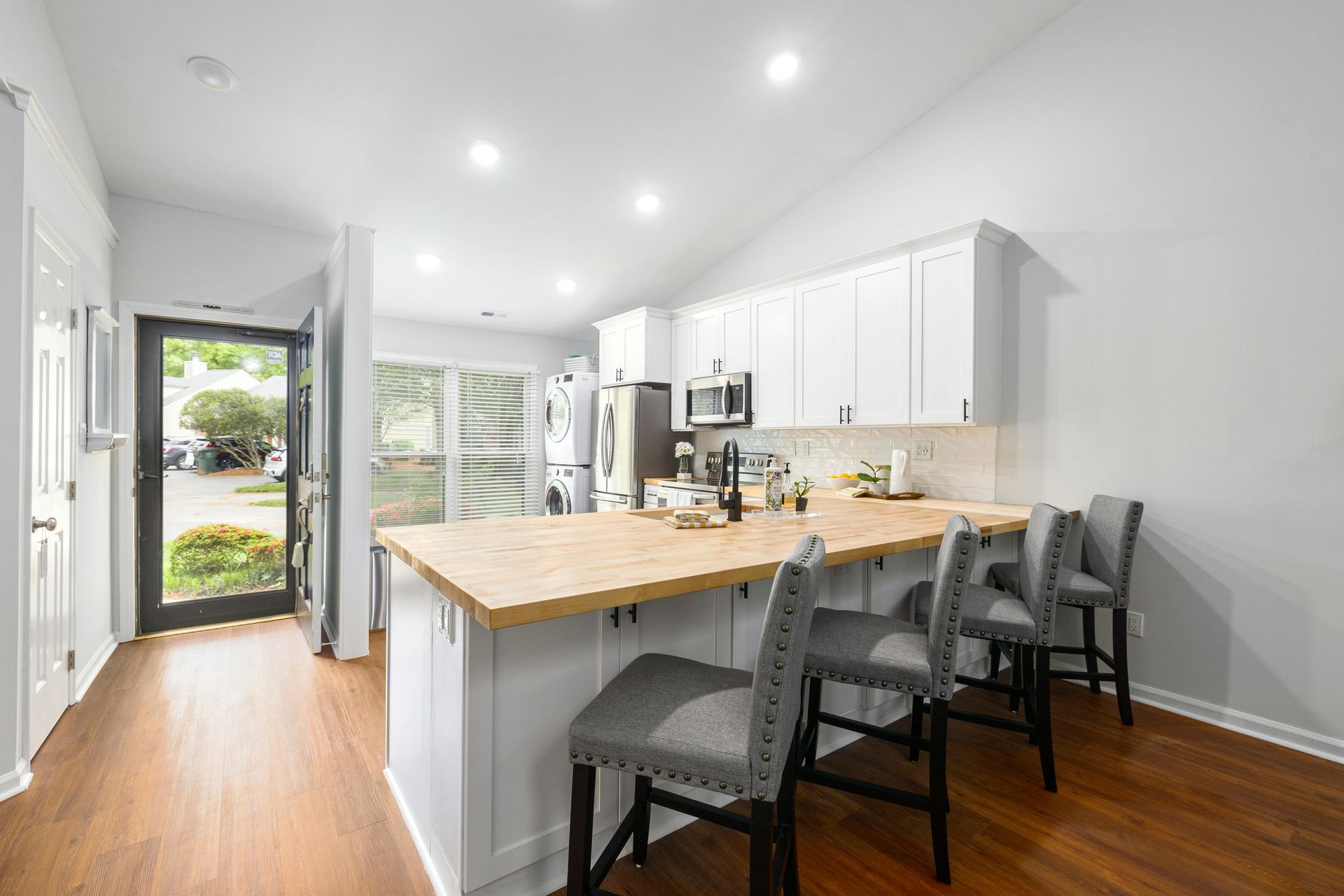 Bright white kitchen with wood floors, island seating, and open front door to the outside
