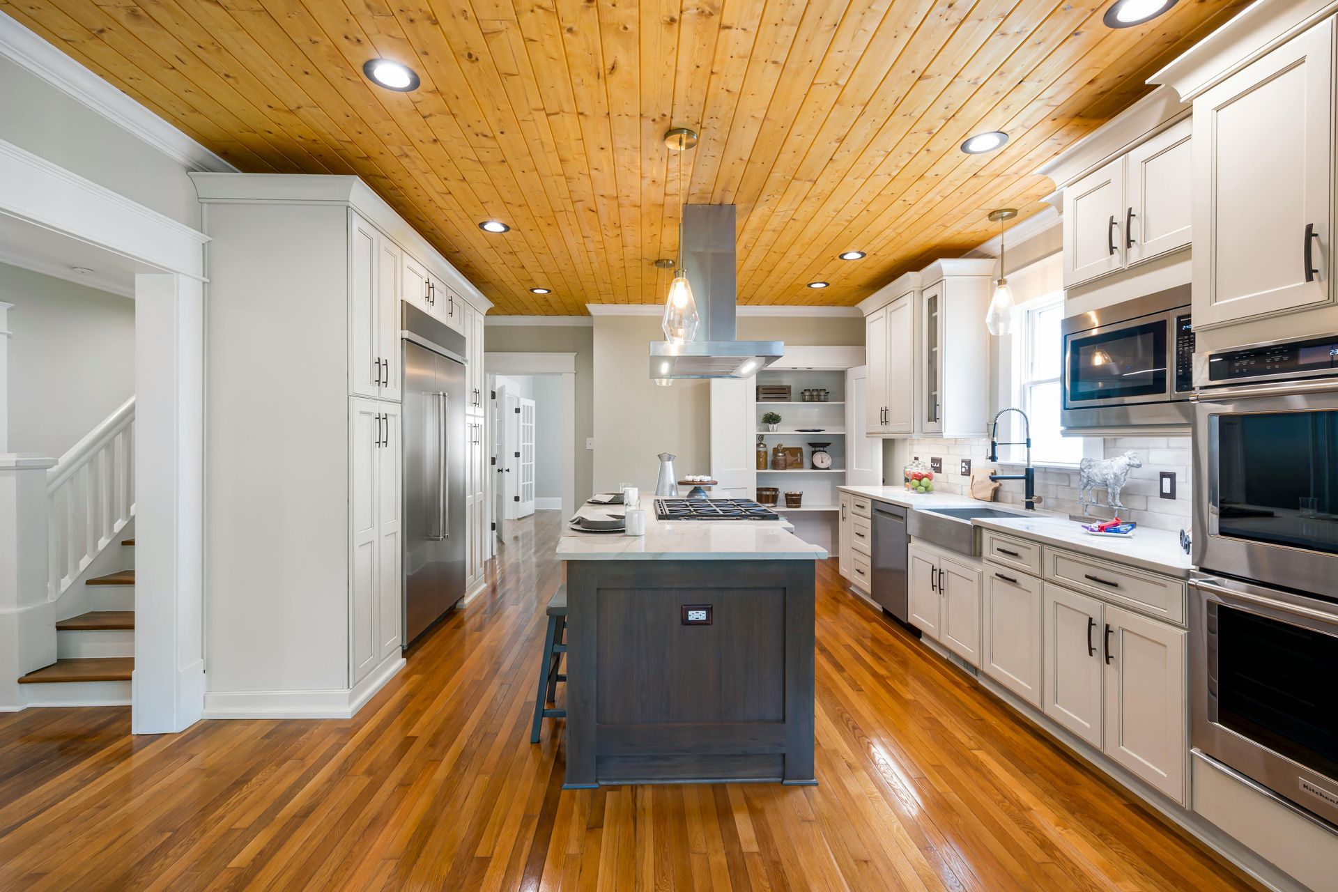 Bright modern kitchen with white cabinets, wood ceiling, stainless appliances, and a central island.