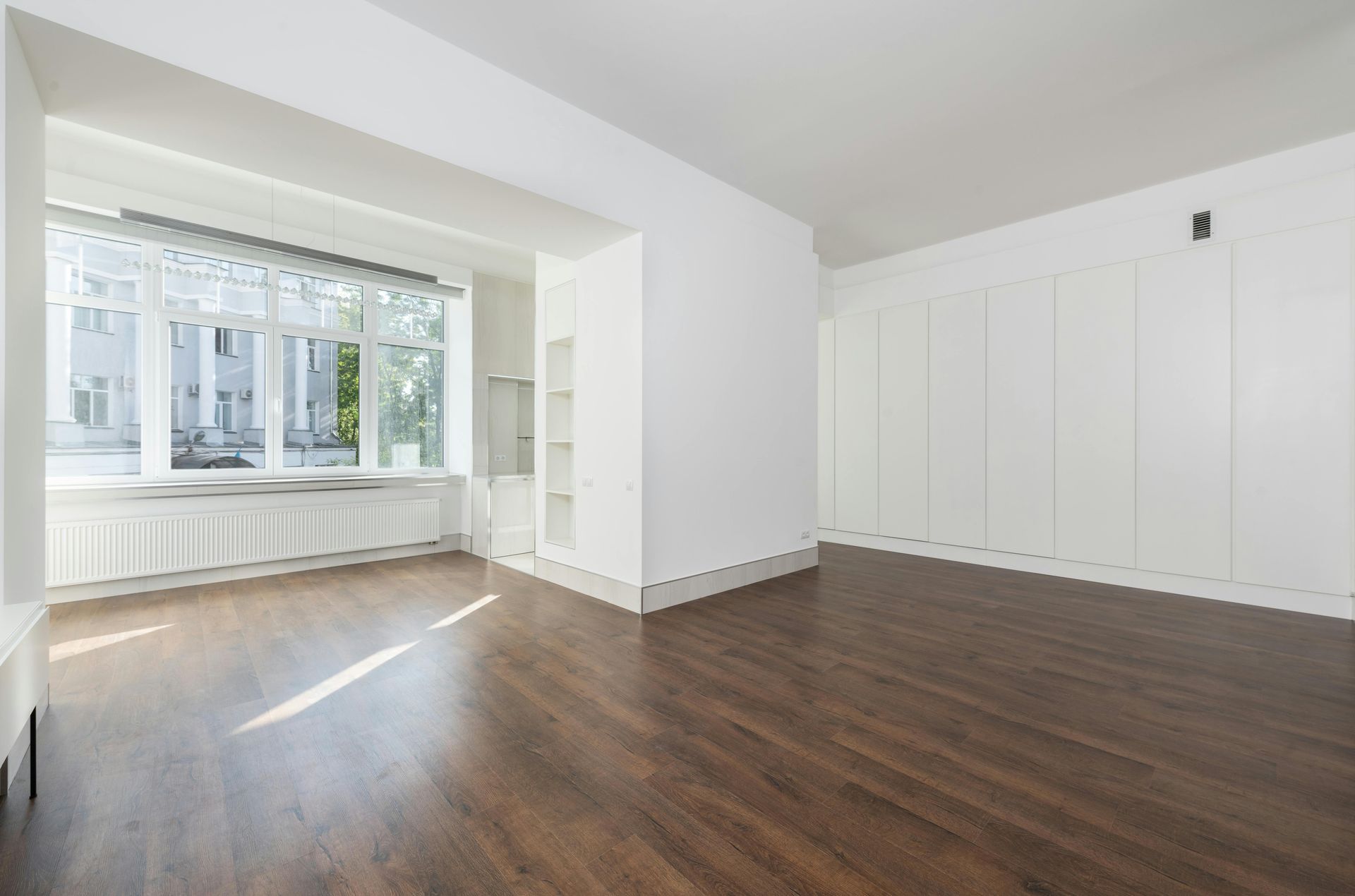 Empty bright room with white walls, dark wood floors, and a large bay window.