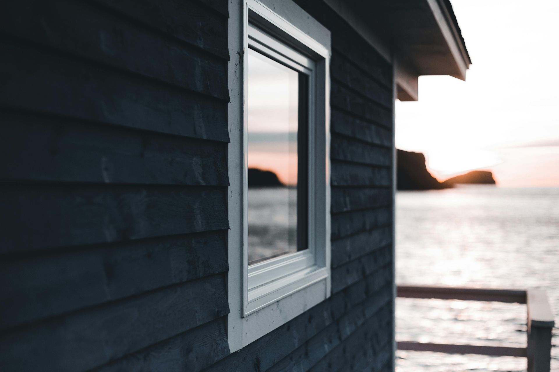 White-framed window on a dark blue house beside a calm waterfront at sunset