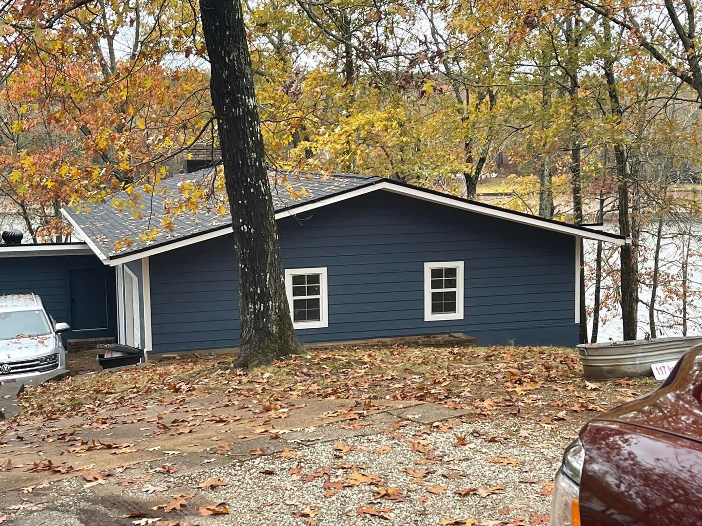 A car is parked in front of a blue house in the woods.