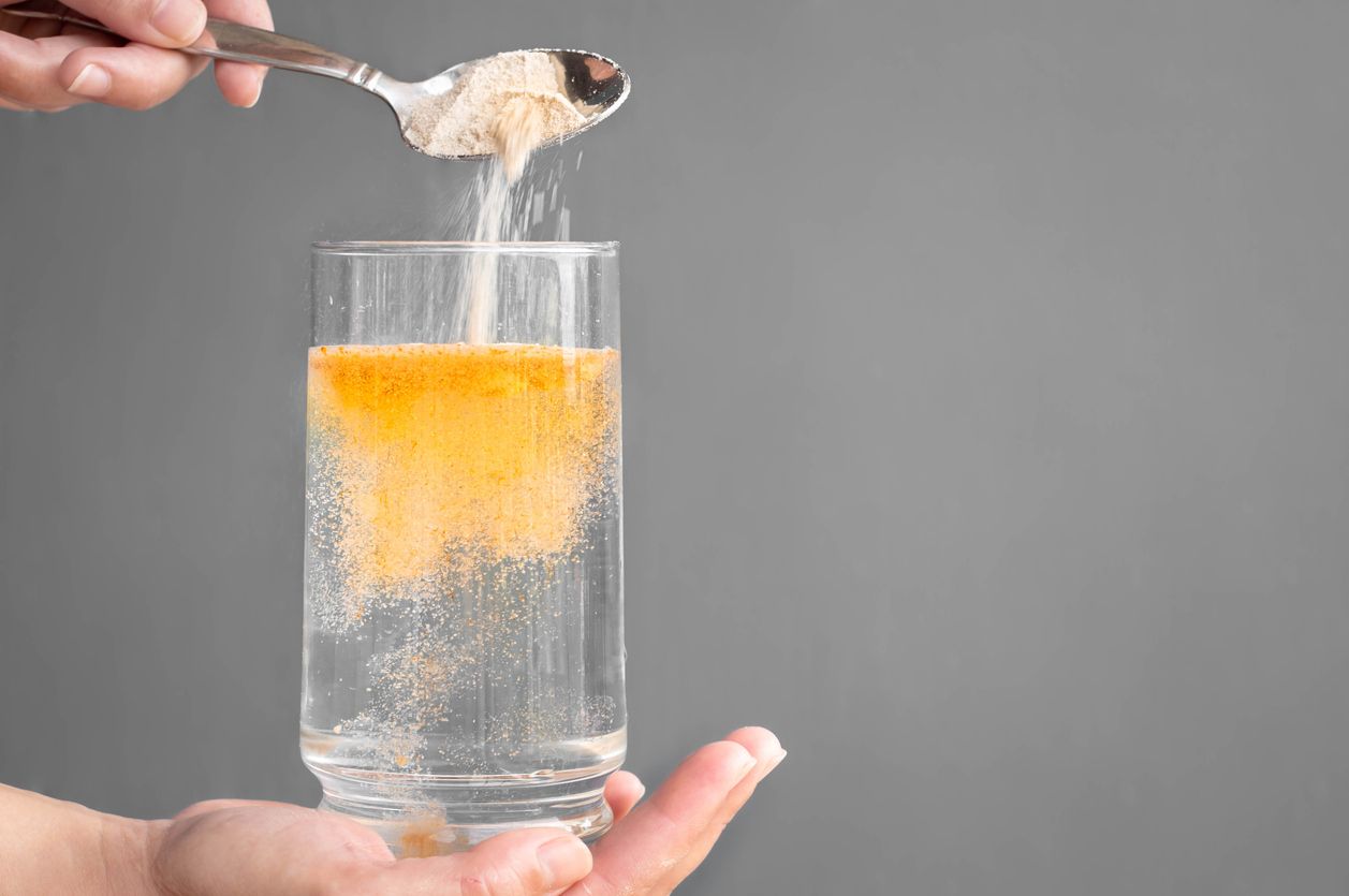 A person is pouring a spoonful of sugar into a glass of water.