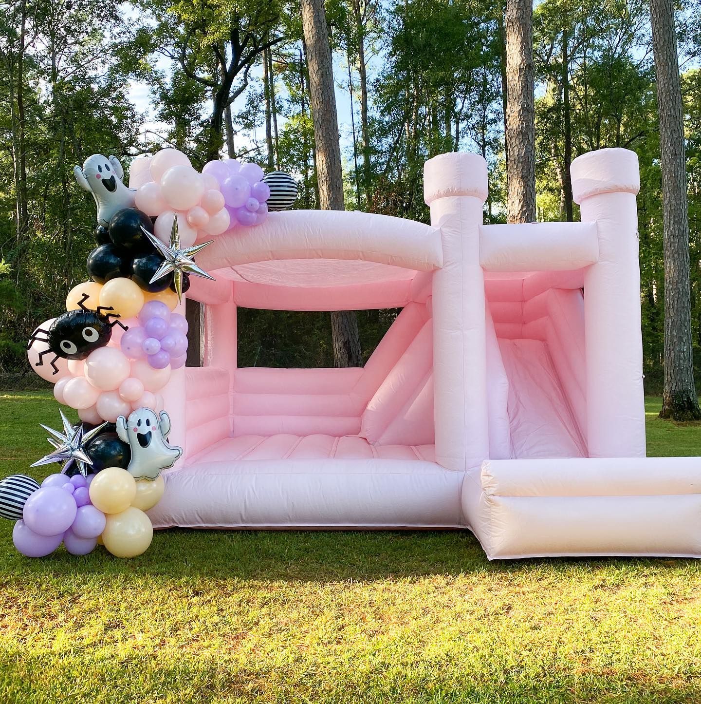 Pink bouncy house with Halloween balloon arch in a grassy yard.