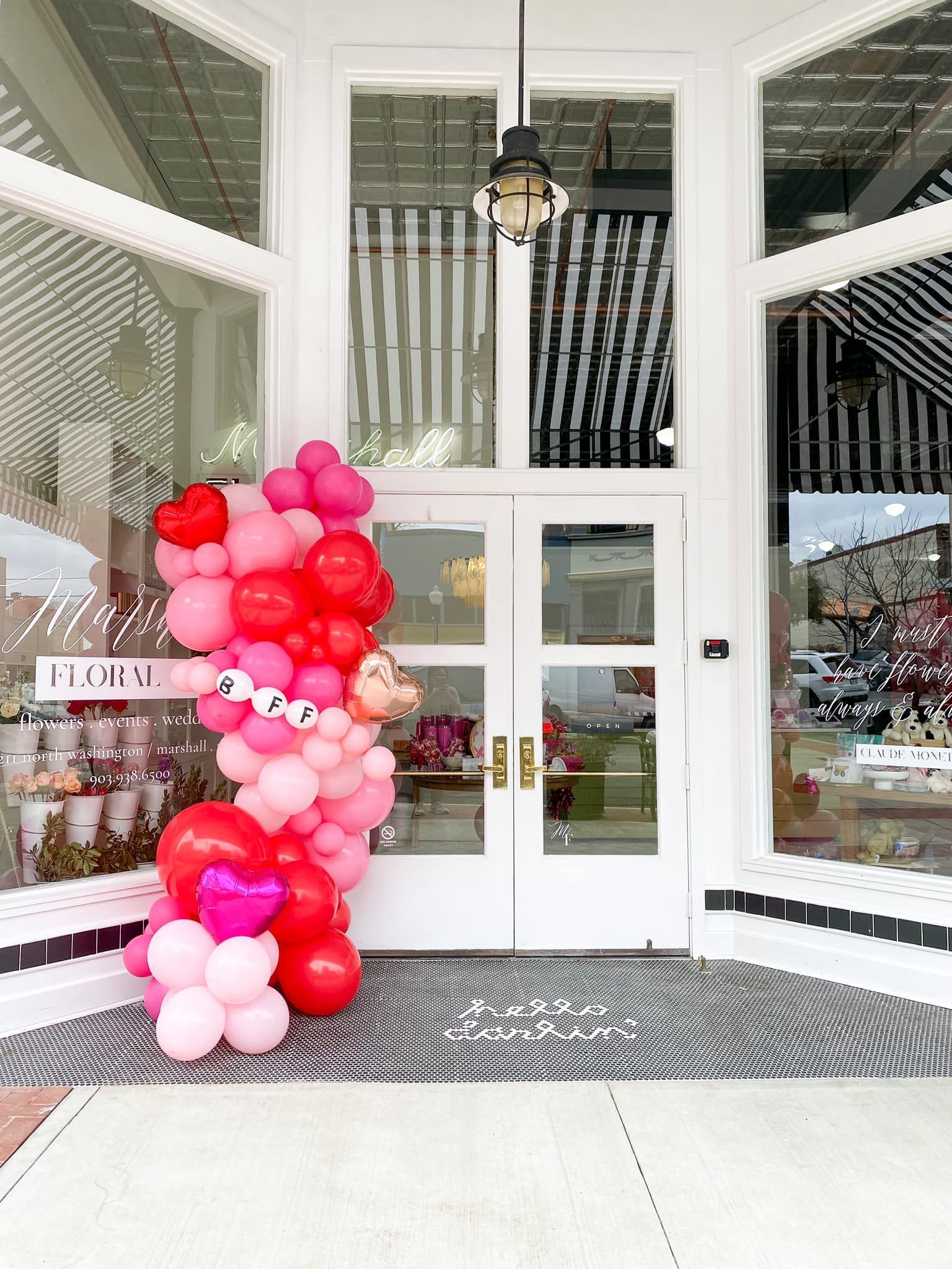 Doorway of a business decorated with a pink and red balloon archway for a celebration.