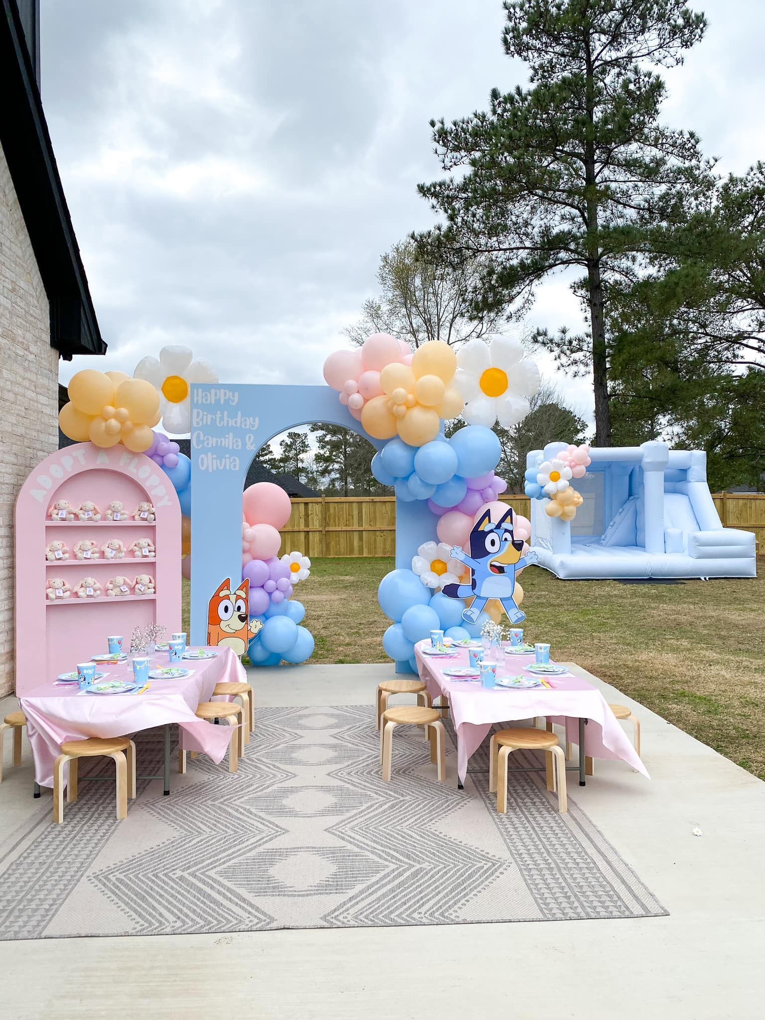 Bluey-themed outdoor birthday party setup: tables, decorations, balloons, bouncy castle, blue and pink.