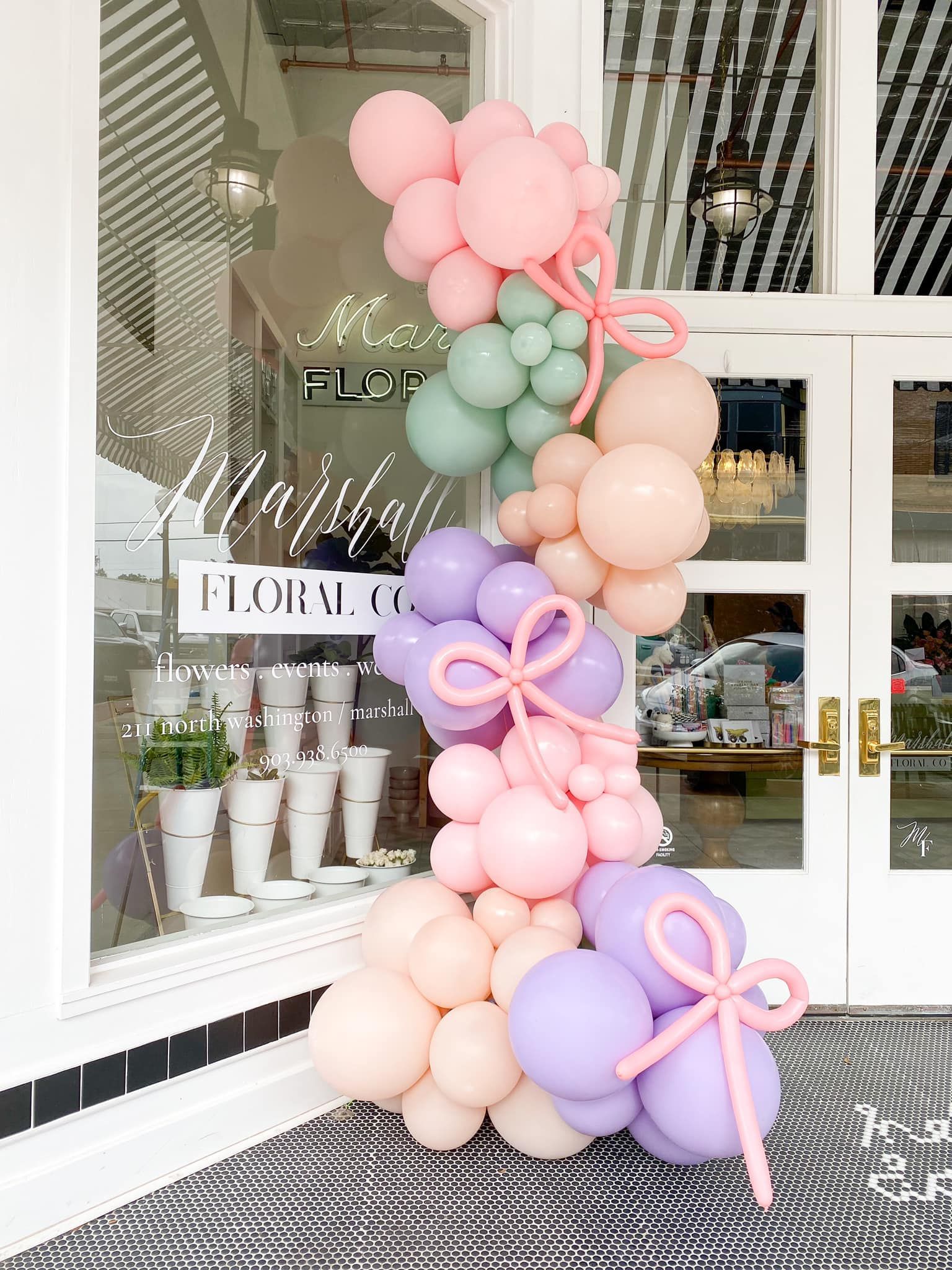 A colorful balloon garland with pink, purple, and mint green balloons draped near a storefront.
