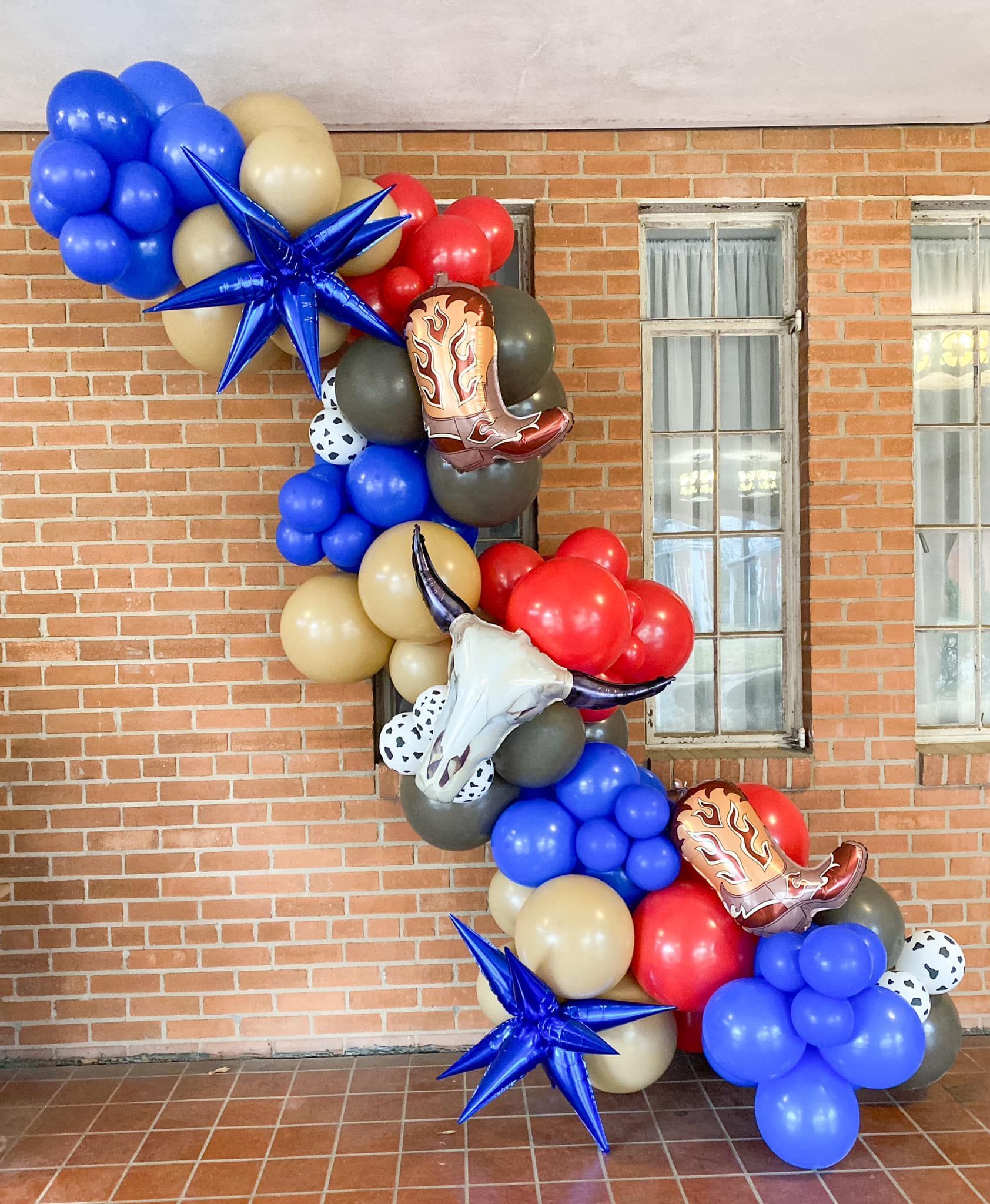 Balloon garland with cowboy boot and star balloons against brick wall.