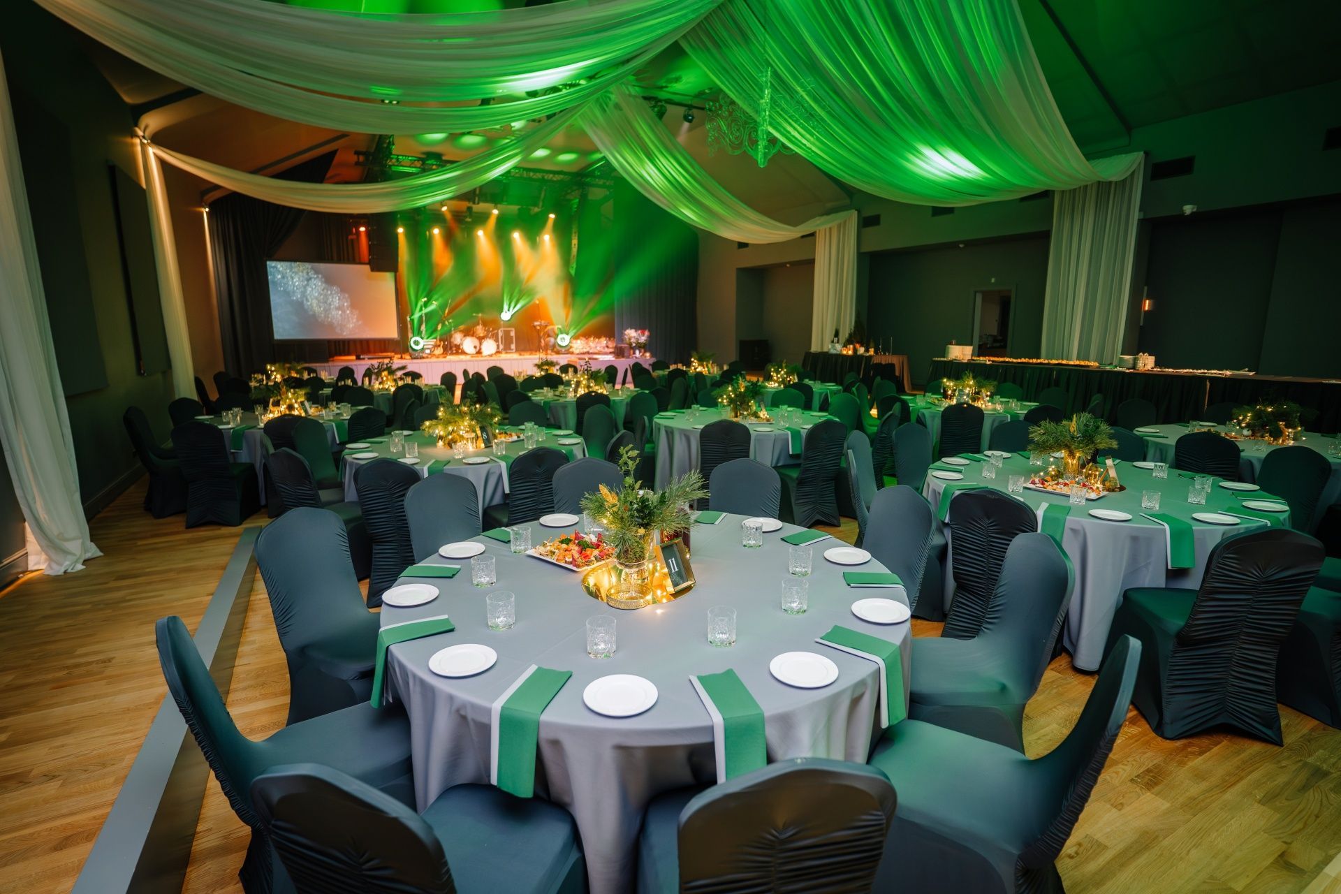 Banquet hall with round tables set for a formal event. Stage in background illuminated with green lights.